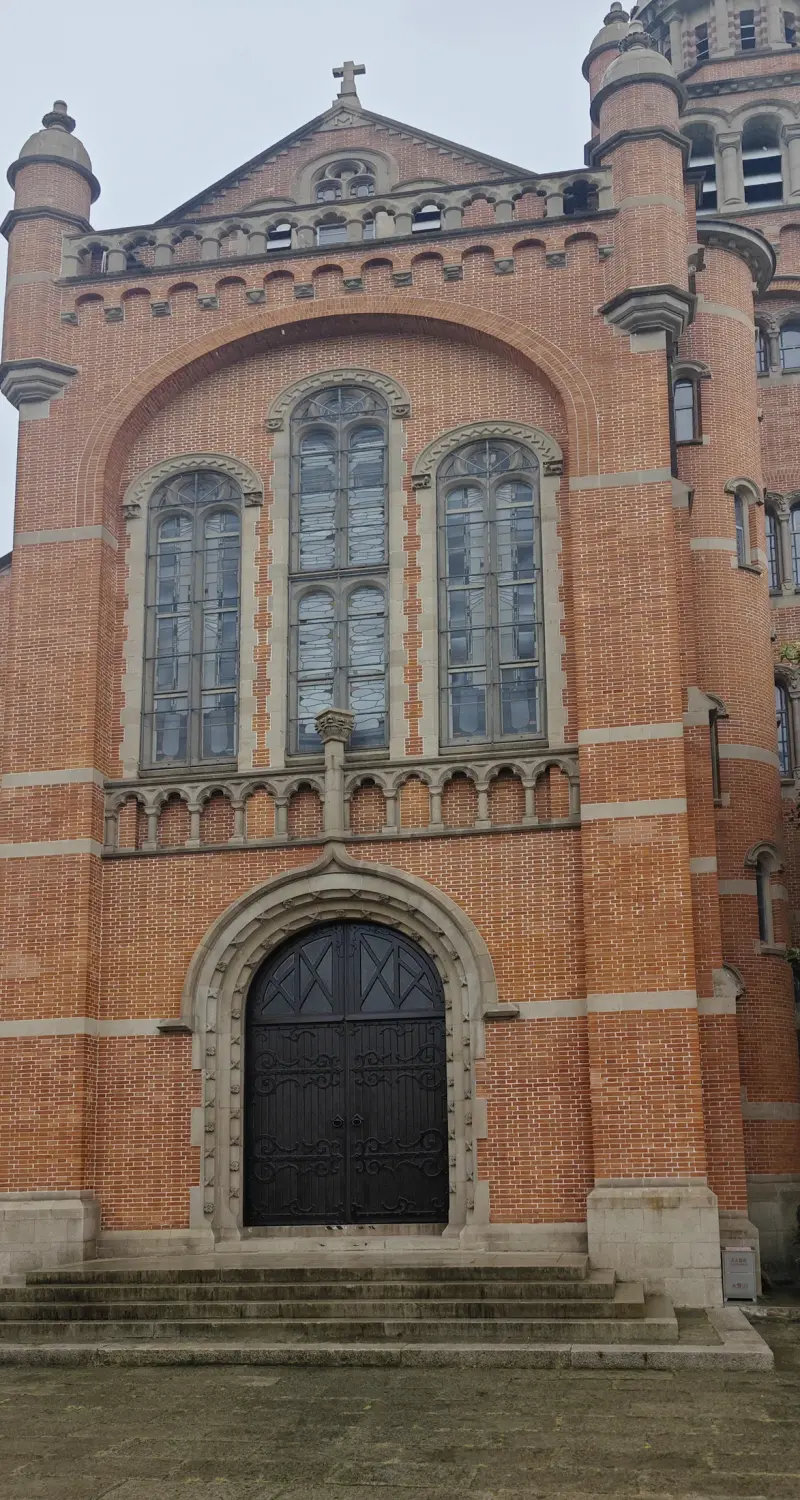 A tall red-brick church front with a deep arched doorway, three narrow arched windows, a gable and a corner tower with turrets.