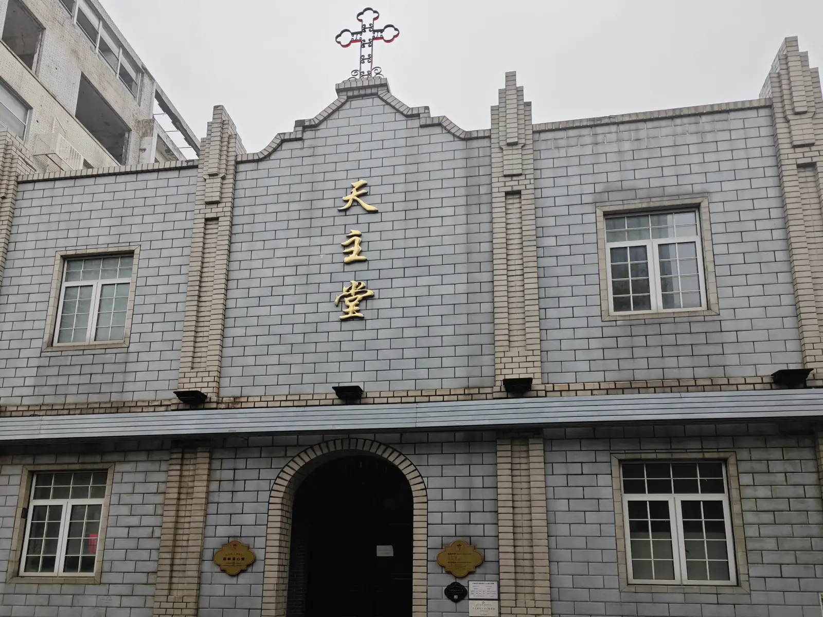 A grey-brick church front with stepped pilasters, a cross, gold Chinese characters and an arched doorway.