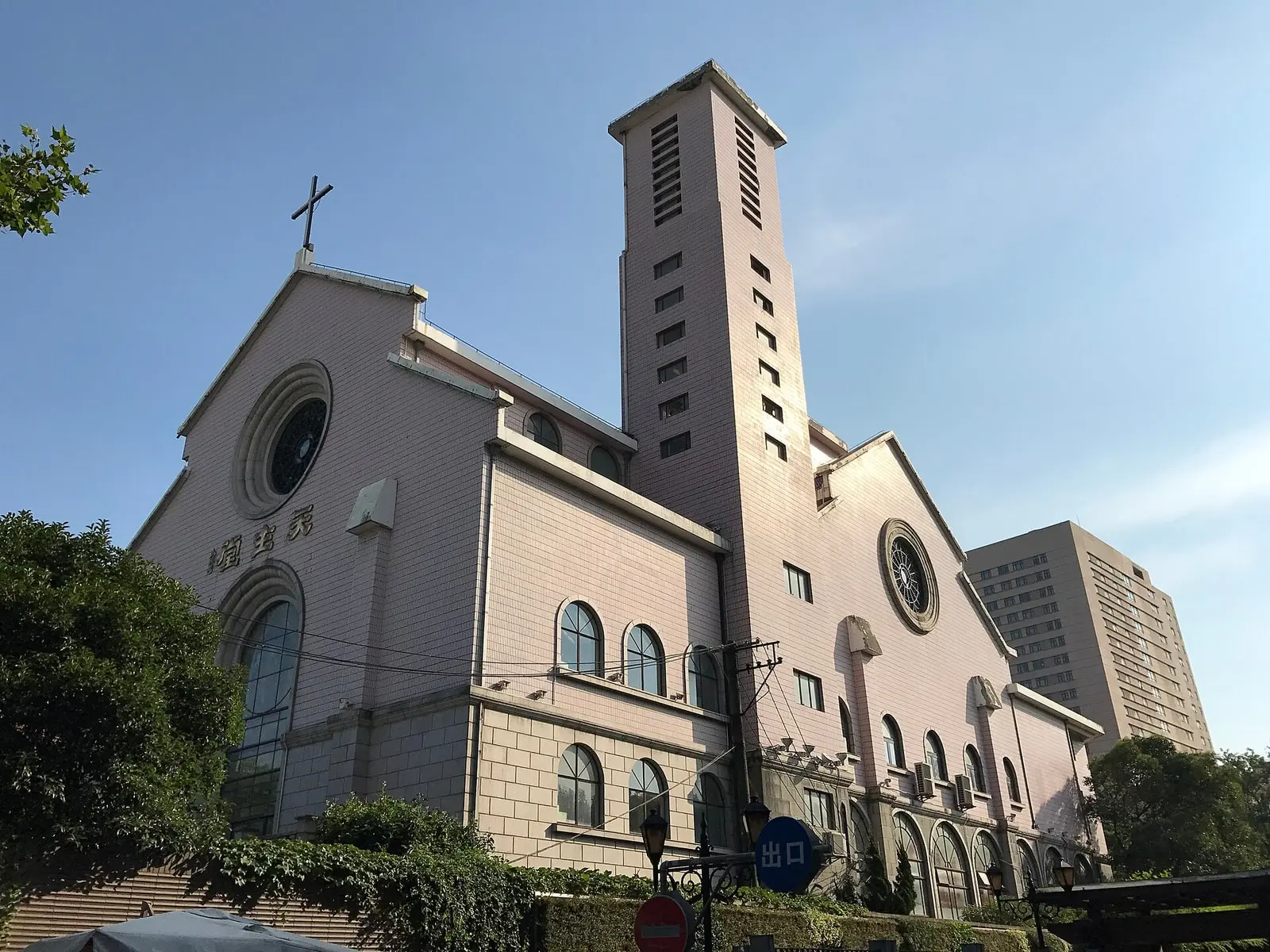 A cream and pink church with a tall slender square tower, round windows and a cross on the gable against a blue sky.