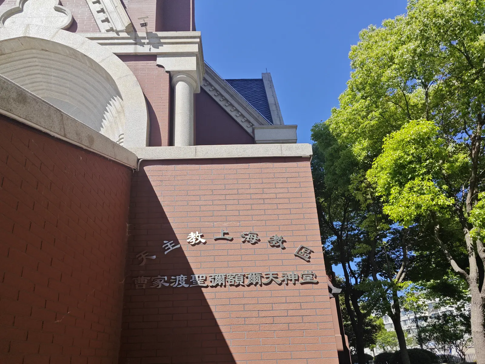 Chinese characters mounted on a red-brick wall corner below the arched stonework of the church.
