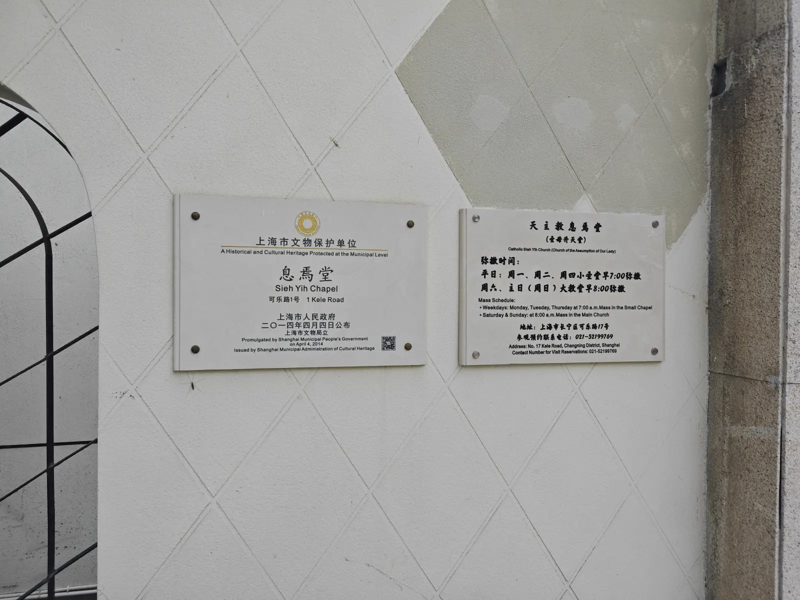 Two wall plaques, one naming a heritage-protected chapel in English and Chinese, the other listing Mass times.