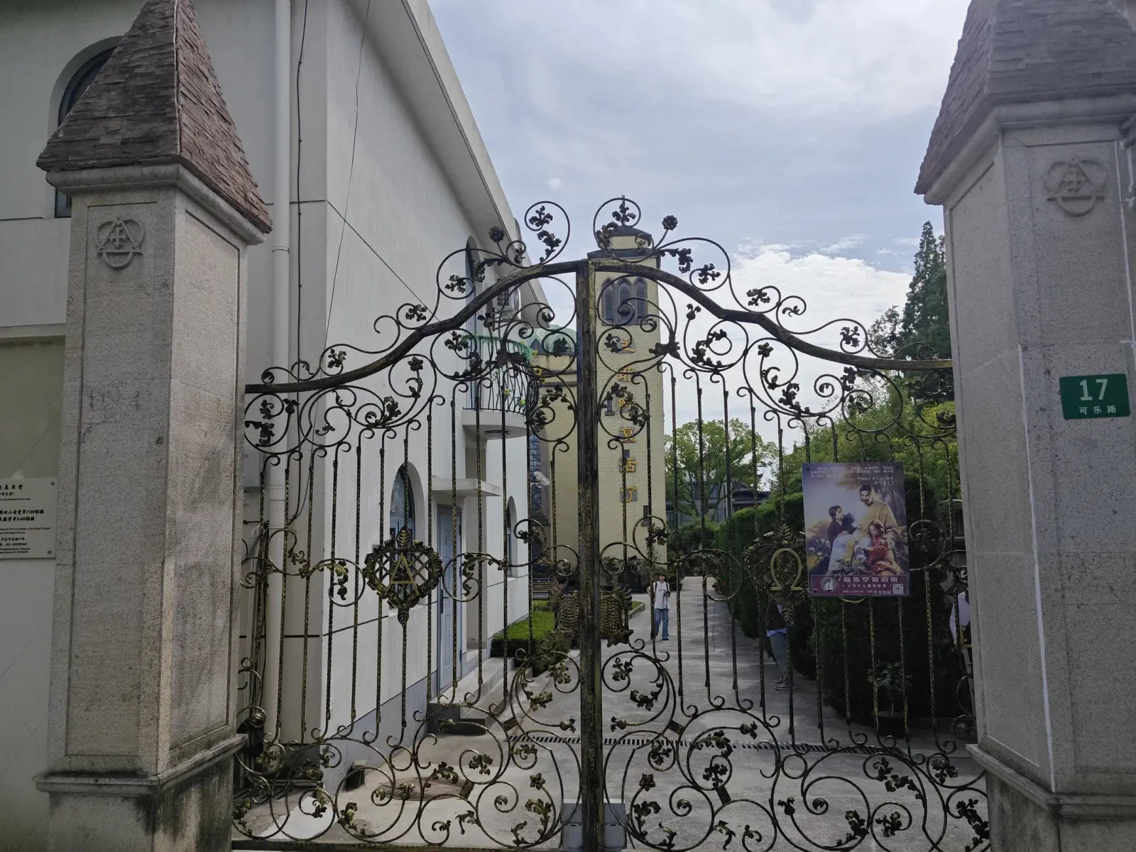An ornate black iron gate between two stone gate piers, with a green number plate.