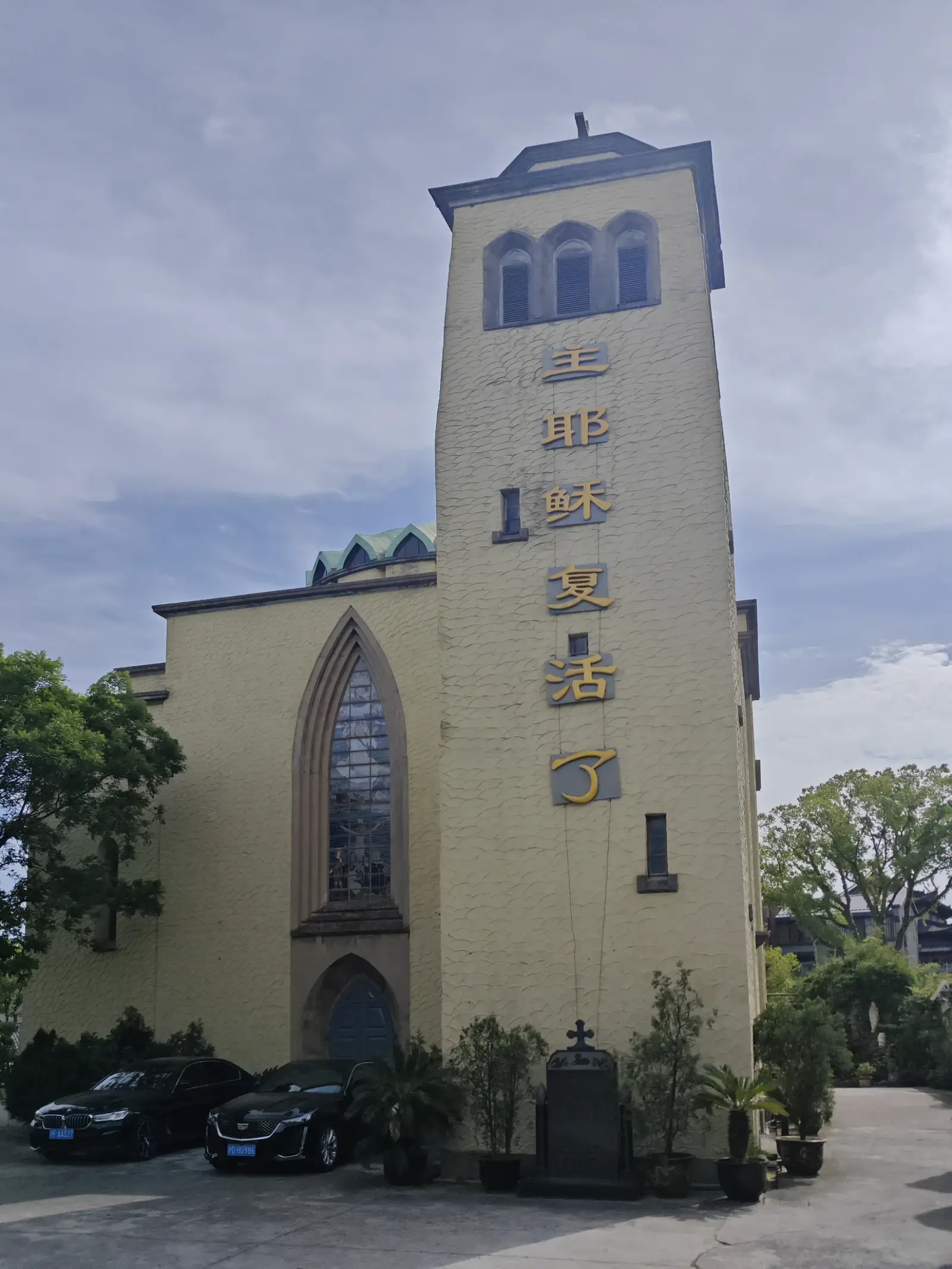 A tall yellow tower with vertical gold characters beside a church wall with a pointed window.