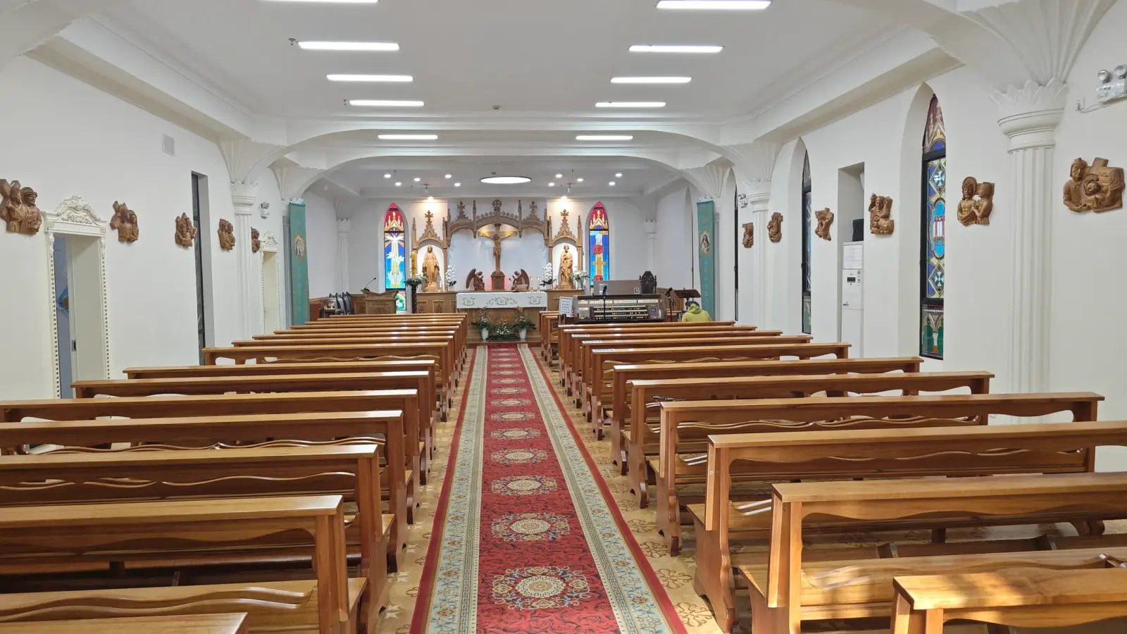 A white-walled church interior with wooden pews along a red carpet toward an altar.