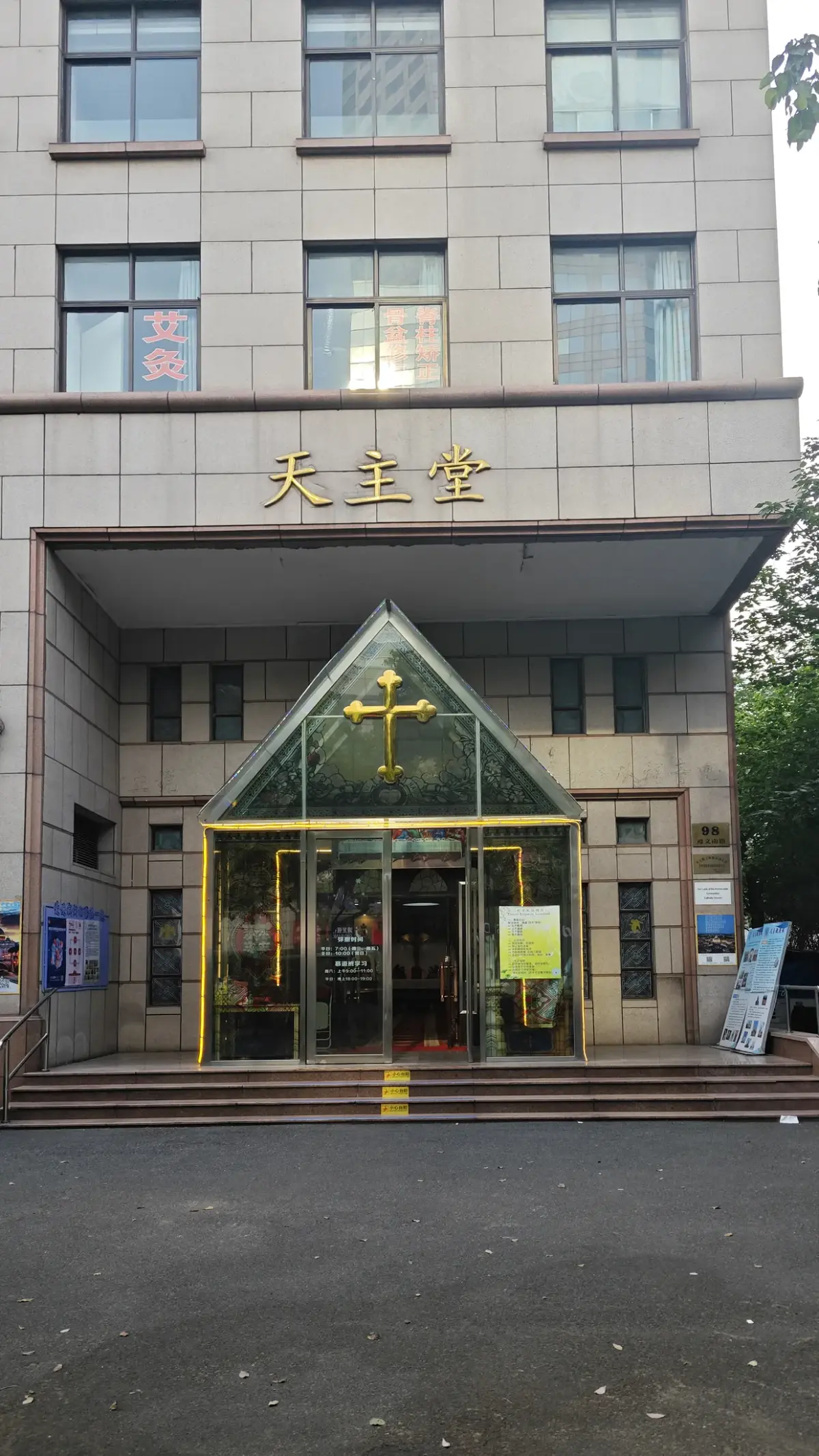 A modern building entrance with a gold cross on a glass canopy and Chinese characters reading Catholic Church above.