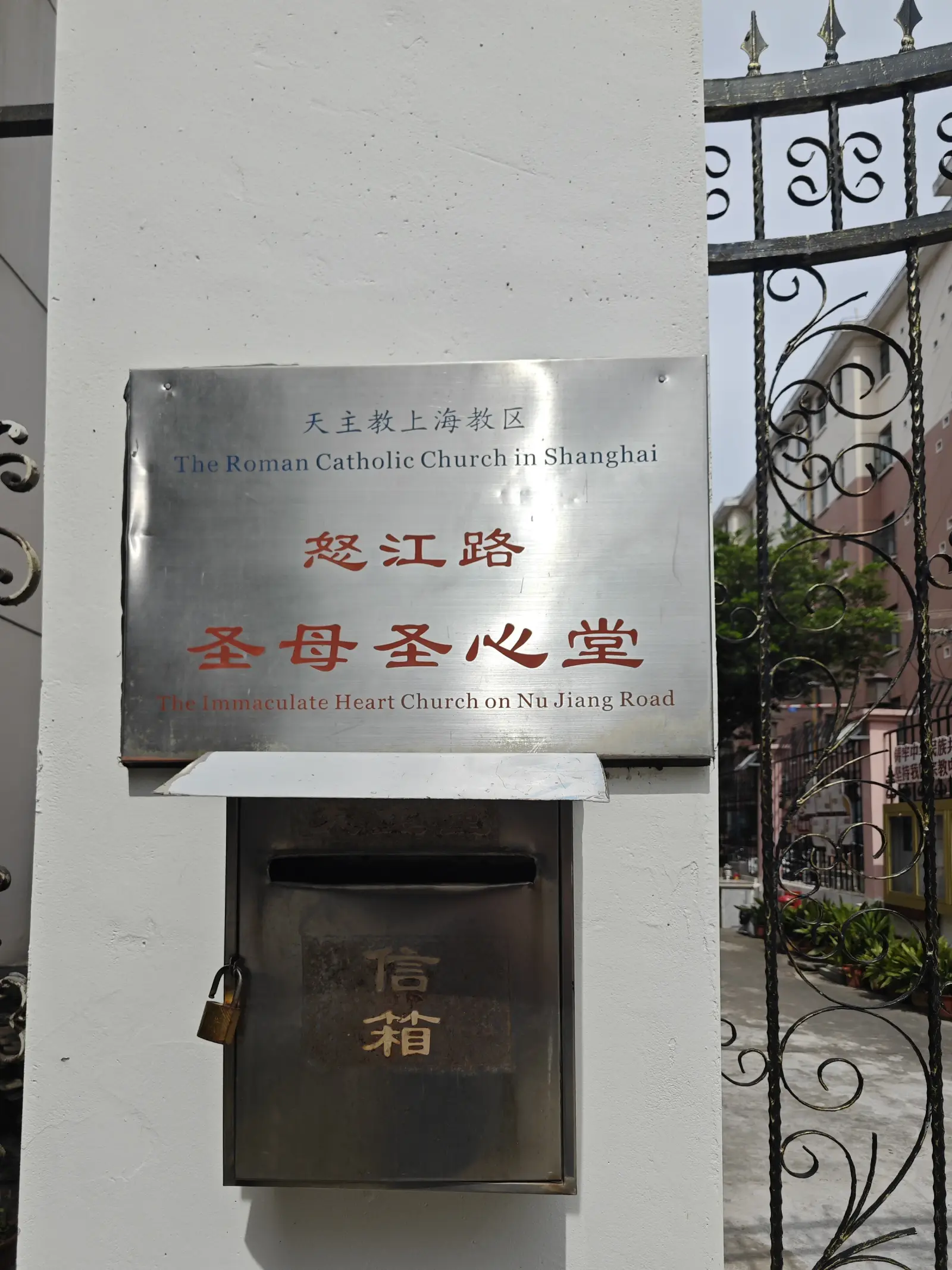 A steel nameplate on a gate pillar with Chinese characters in red and a line of small English text.