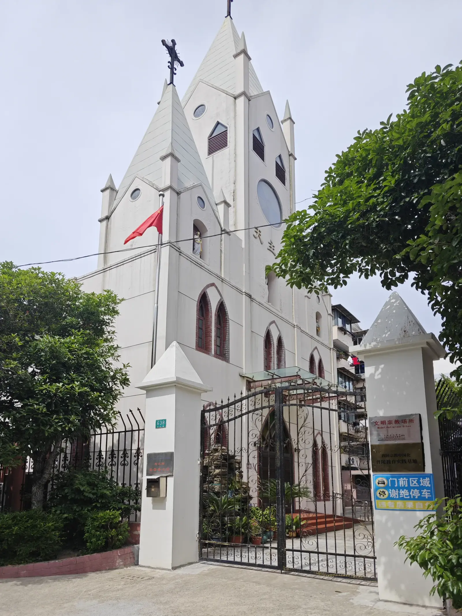 A white Gothic-style church front behind an iron gate and trees.