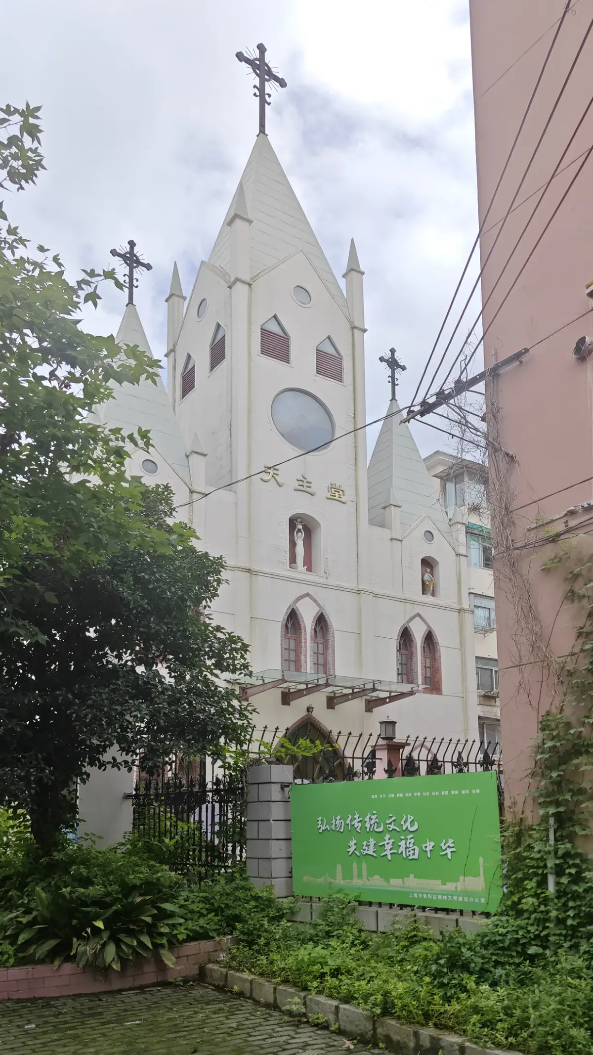 A white church front with spire seen over greenery and a green banner.