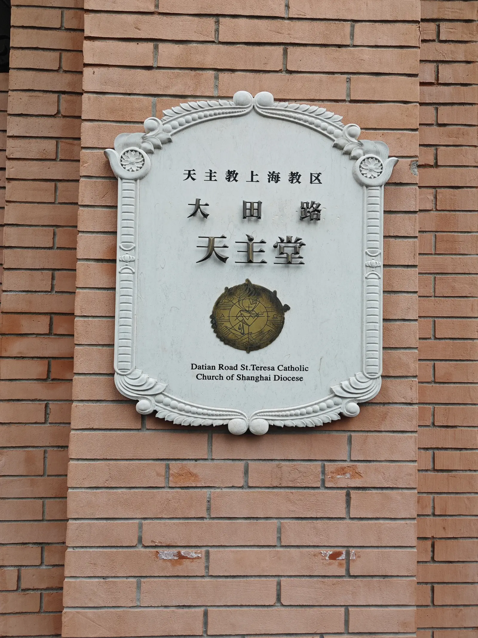 A scrolled white plaque on a brick wall with Chinese characters and a small English line.