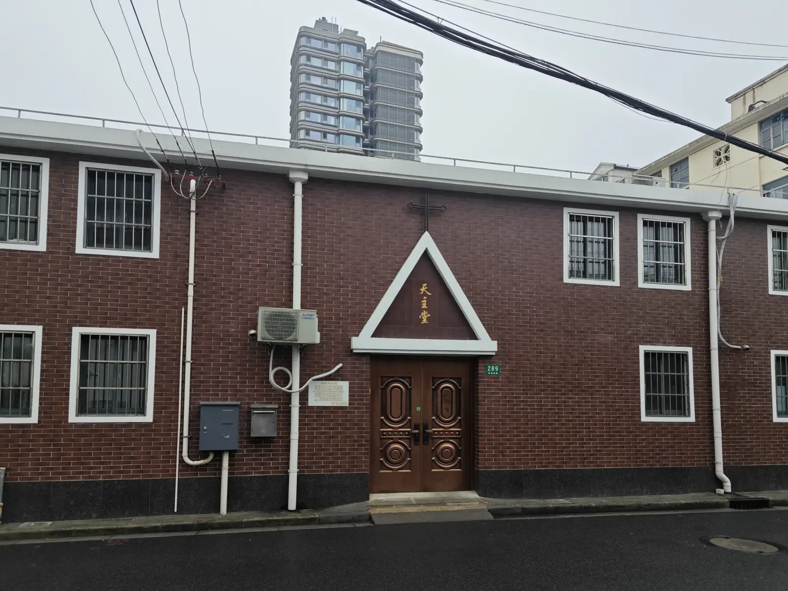 A red-brick two-storey building with barred windows and a wooden door under a white triangular porch.