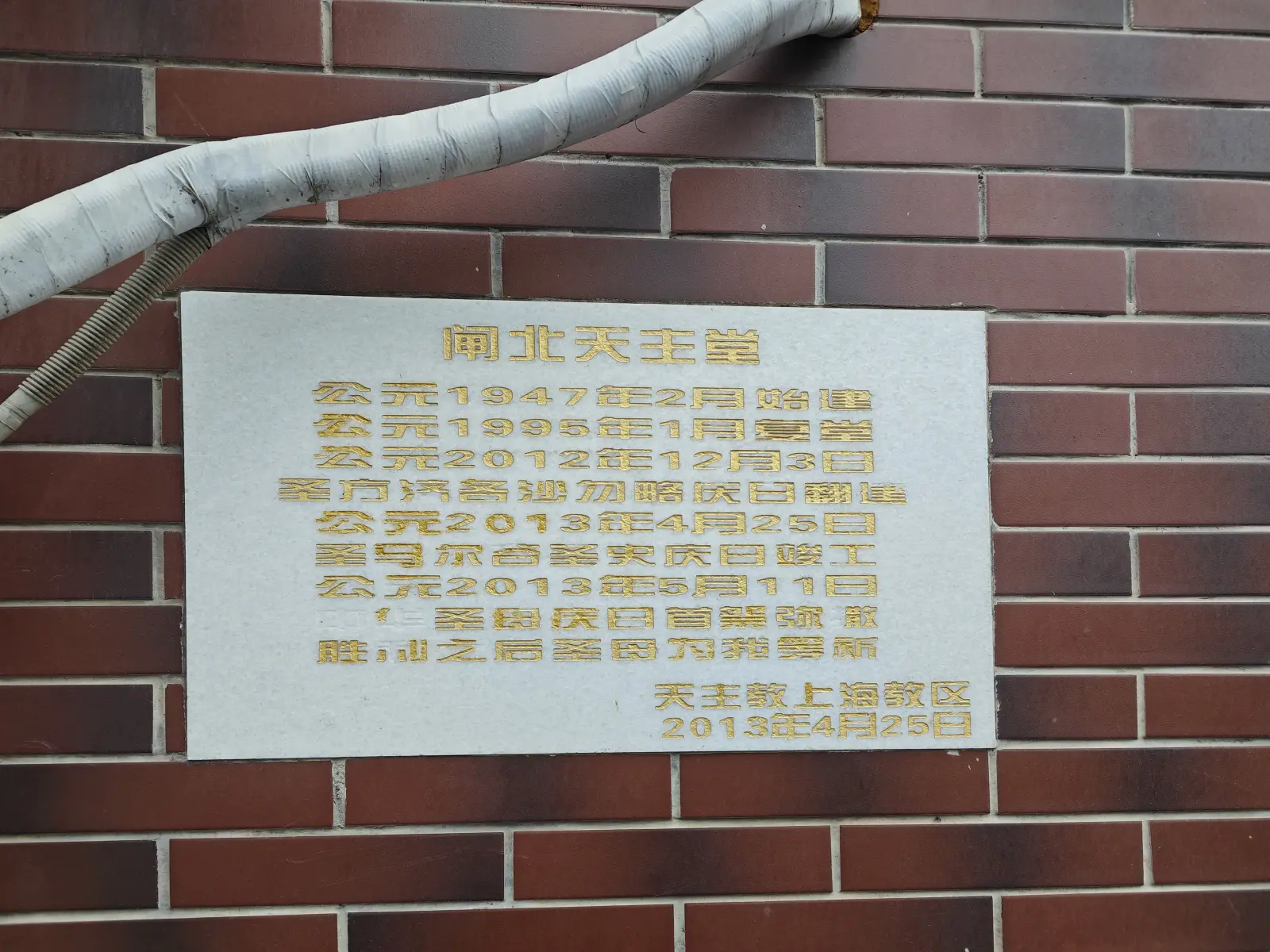 A white stone plaque with gold Chinese characters set in a red-brick wall.