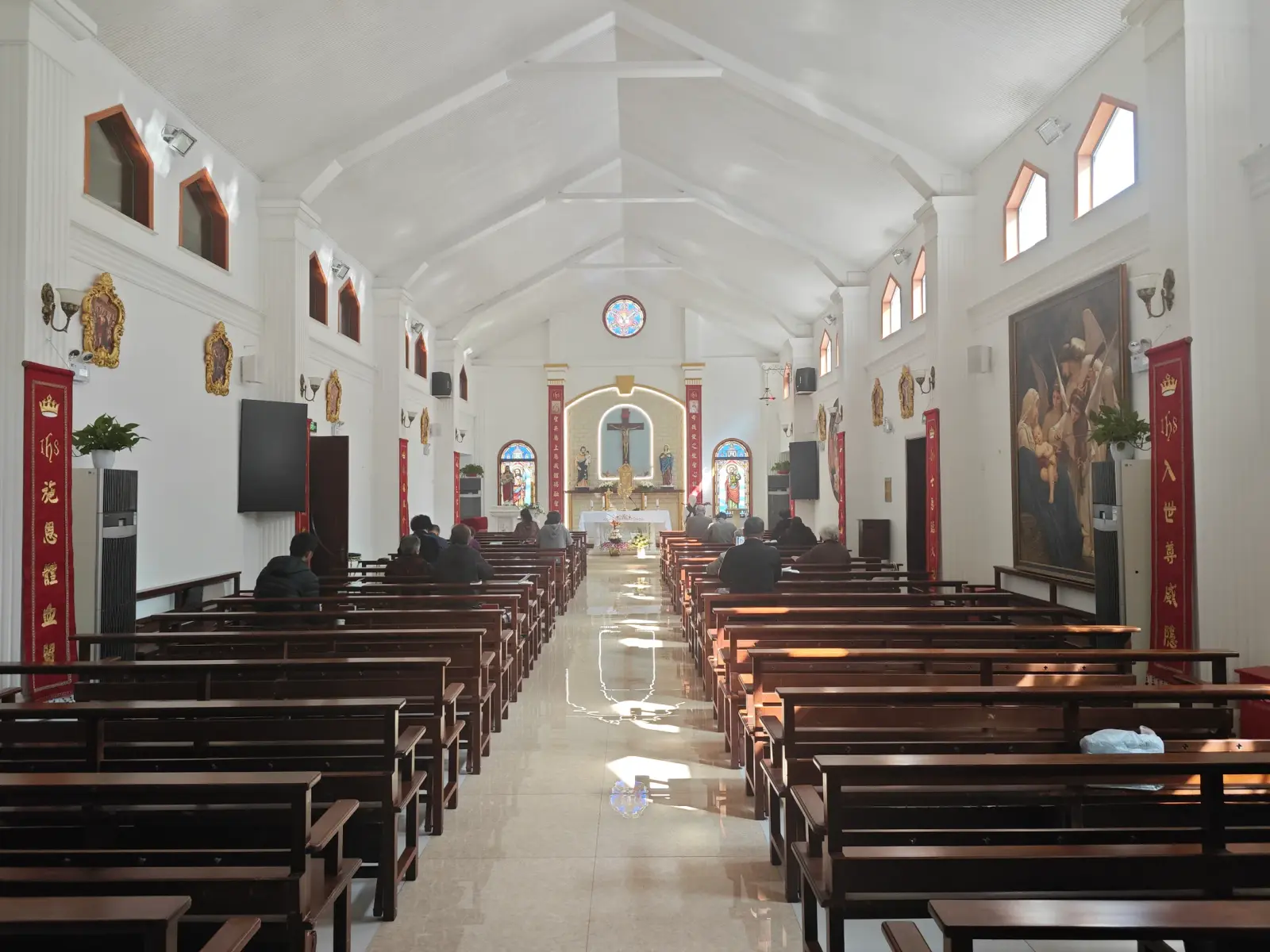 A church interior with wooden pews, white walls and a crucifix at the far end.