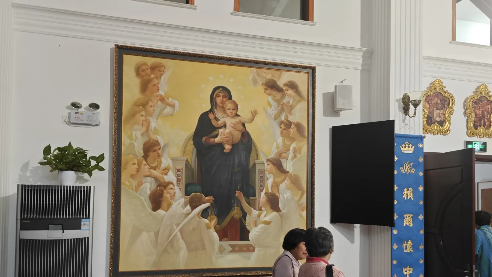 A big framed painting of a Madonna with child and angels beside blue banners.