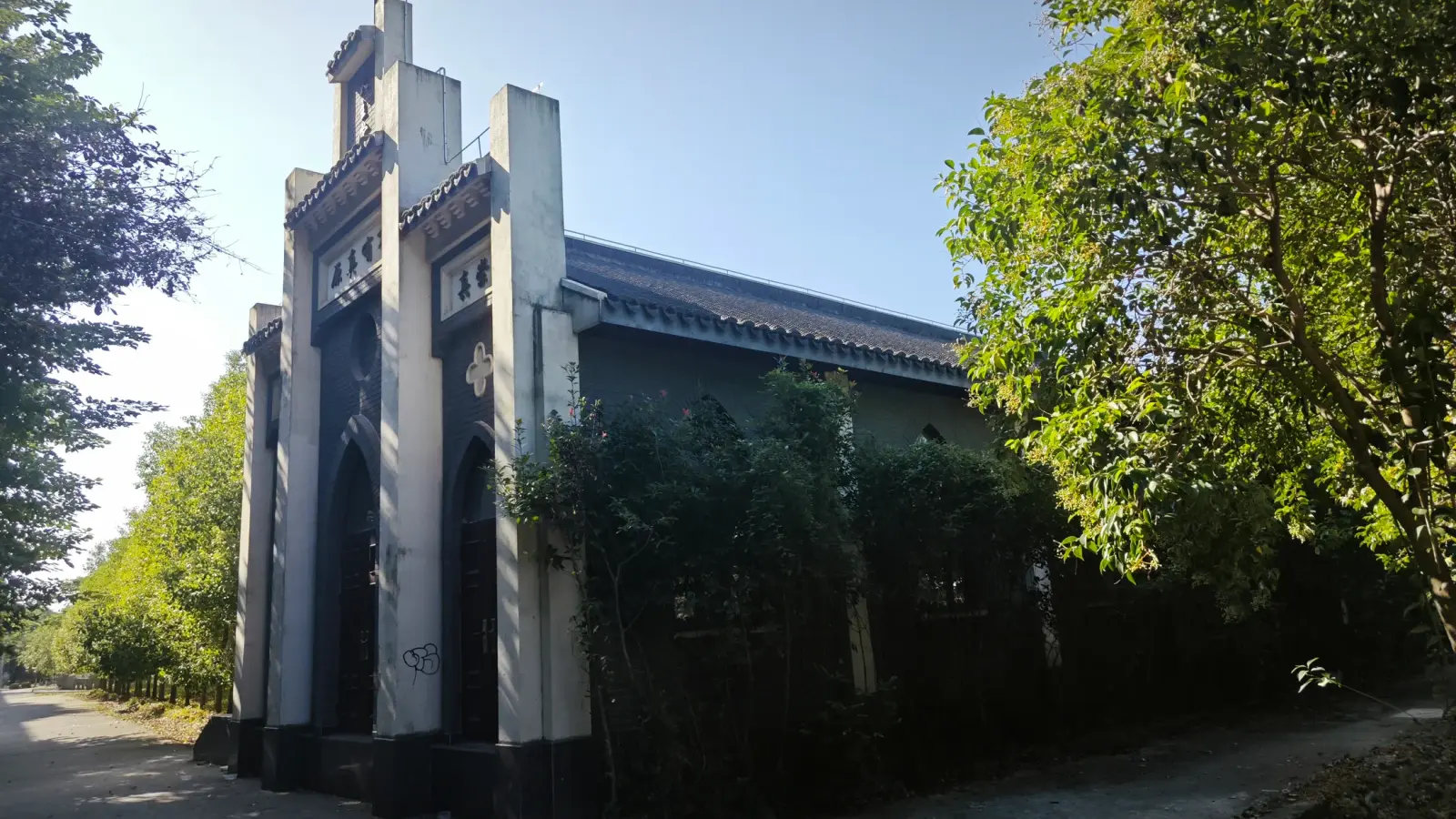 A grey and white church gable with stepped pilasters beside a footpath and trees.
