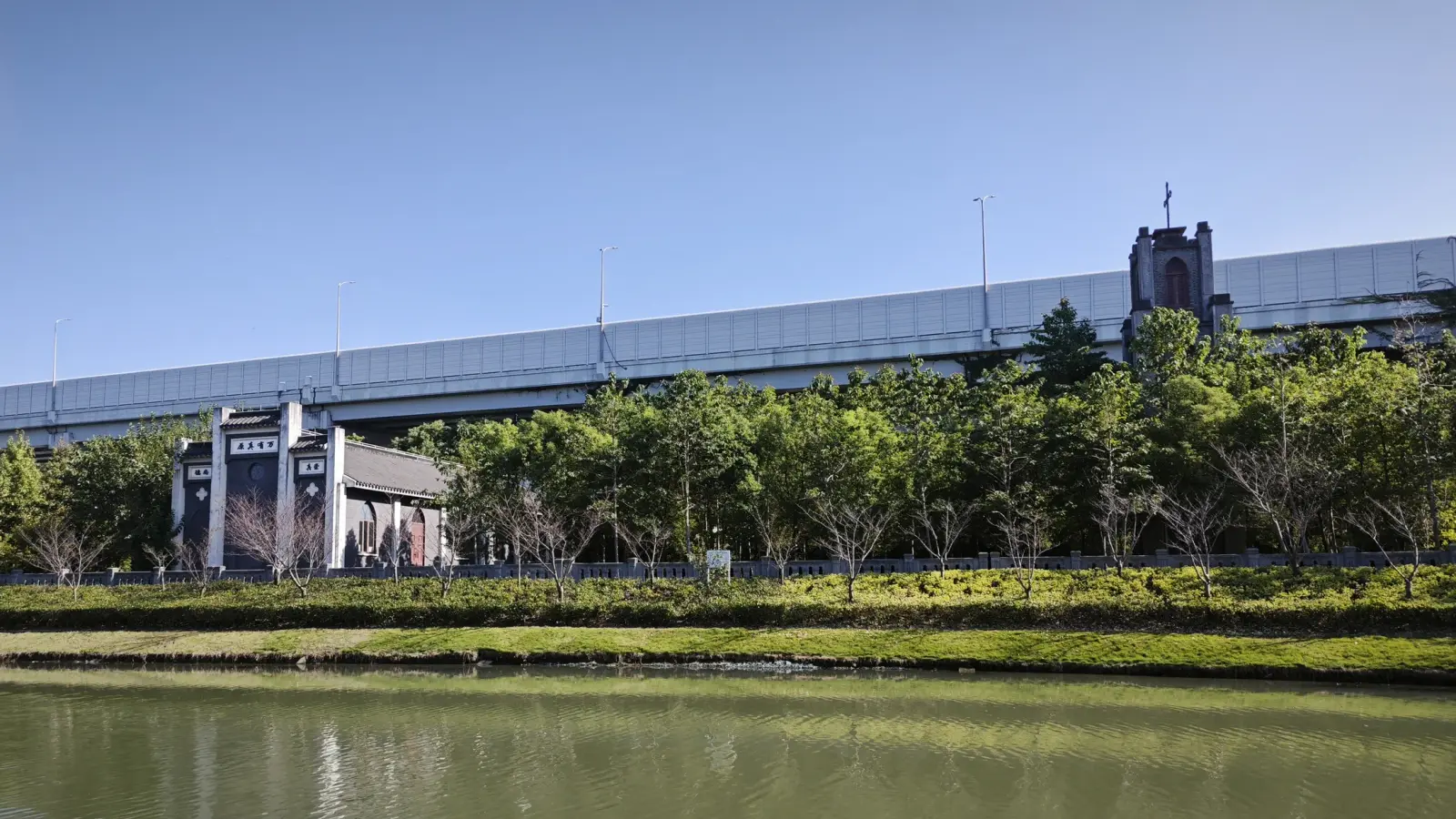 A canal bank with a small church front and a long elevated road behind it.