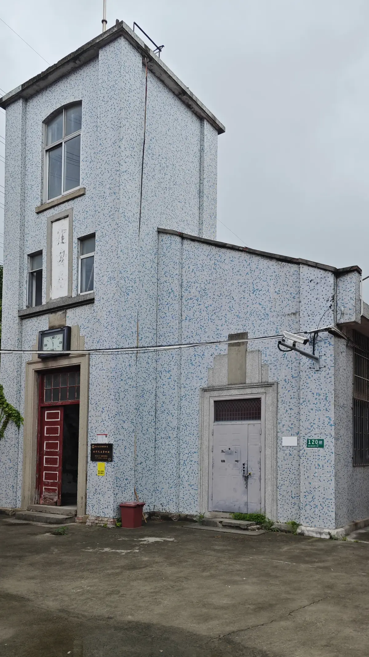 A narrow square tower covered in small blue and white tiles with a red doorway at the base.