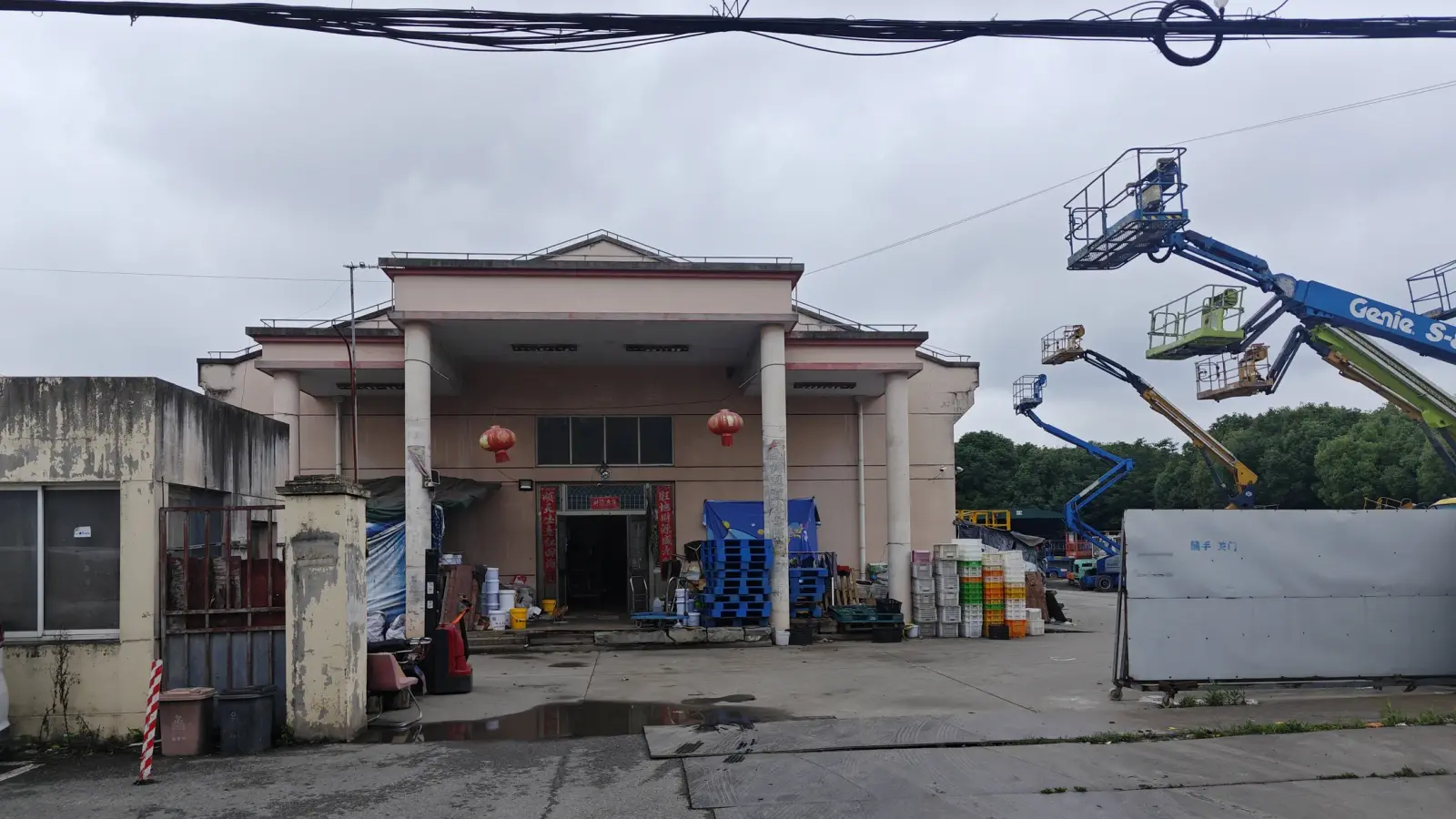 A single-storey building with a columned porch and red lanterns, with boxes and lifting platforms around it.