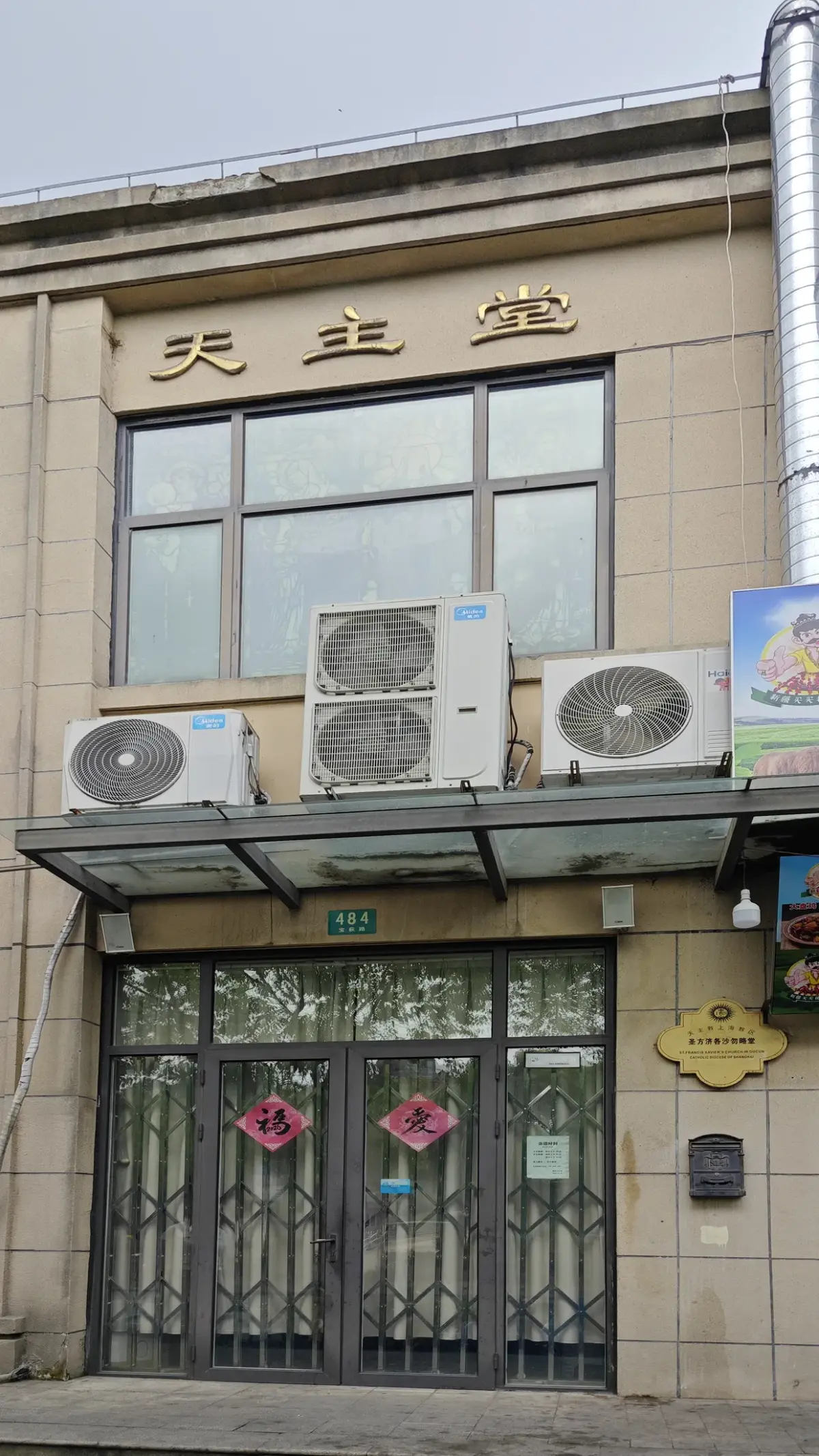 A grey metal gate under a church name in the upper wall of a beige building.