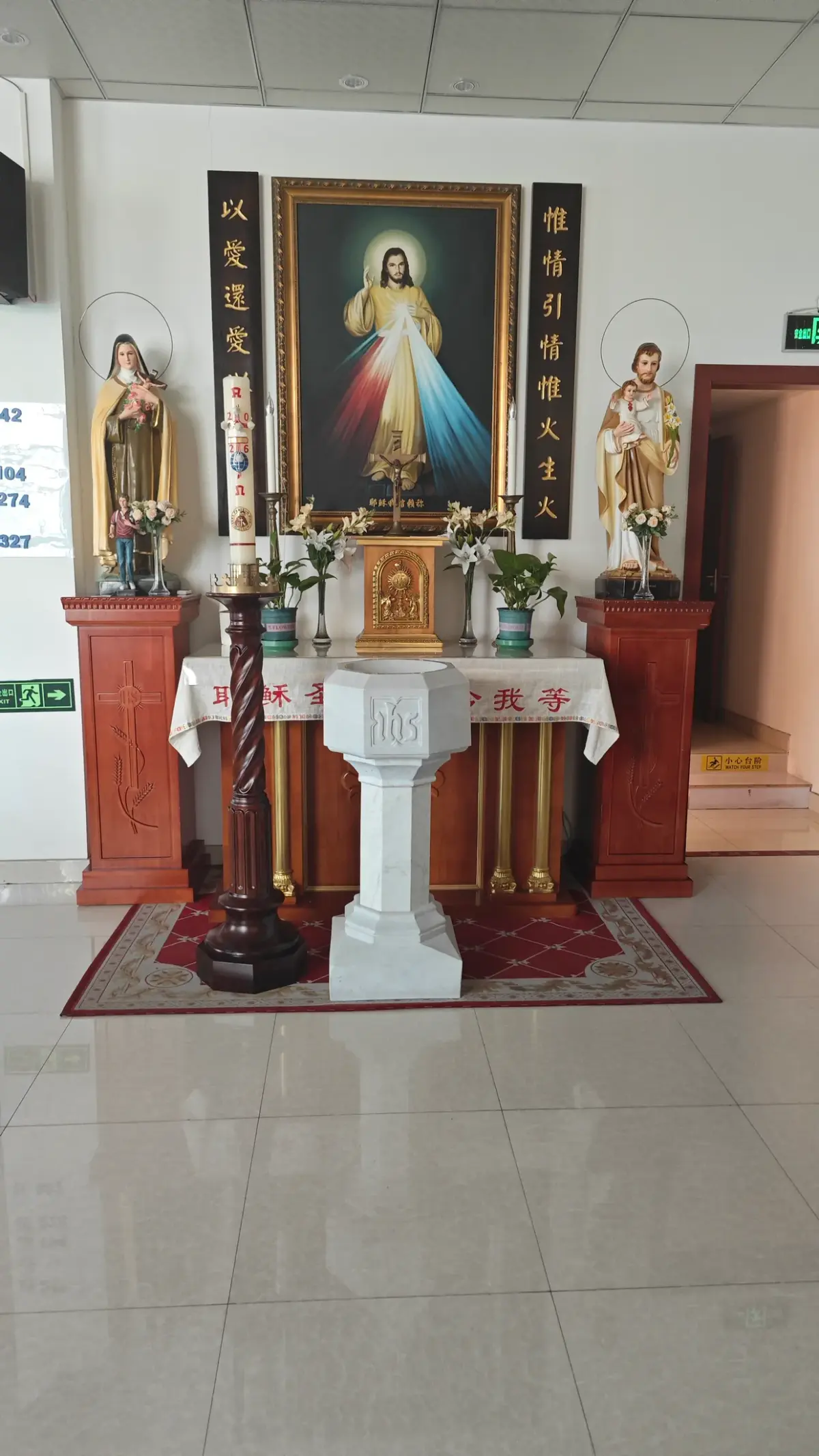 A framed painting of Christ with rays of light between two saints' statues above a small table.