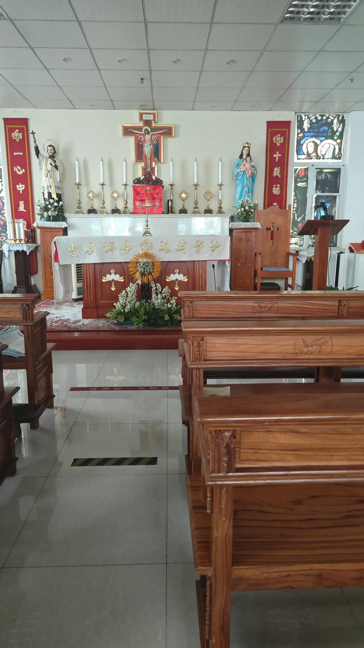 A bright room with wooden pews leading to an altar with candles and a crucifix.