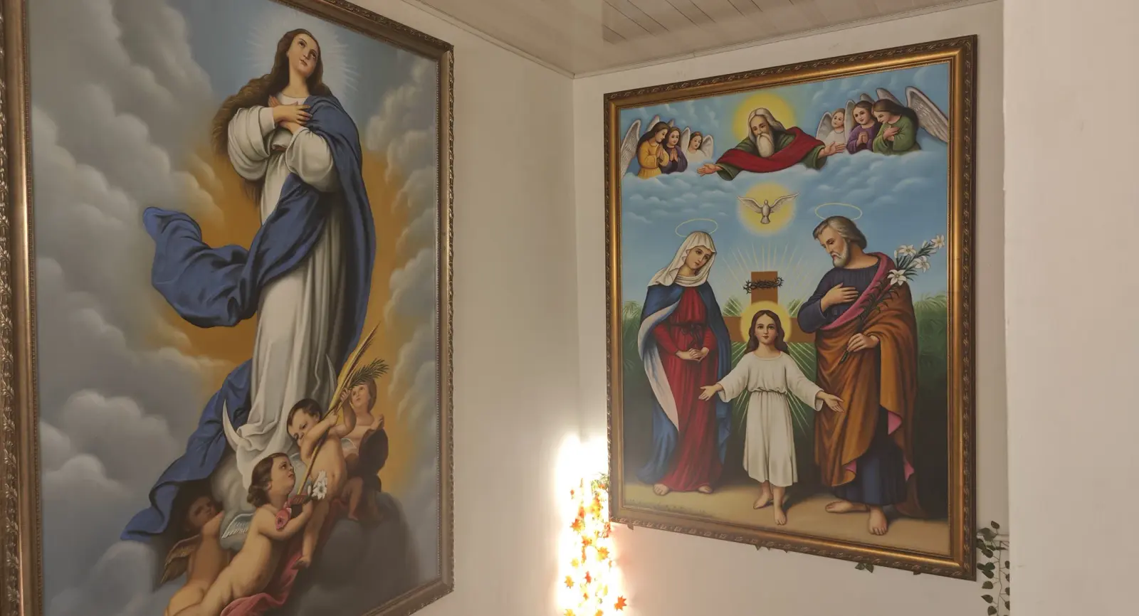 Two framed religious paintings on a white corner wall.