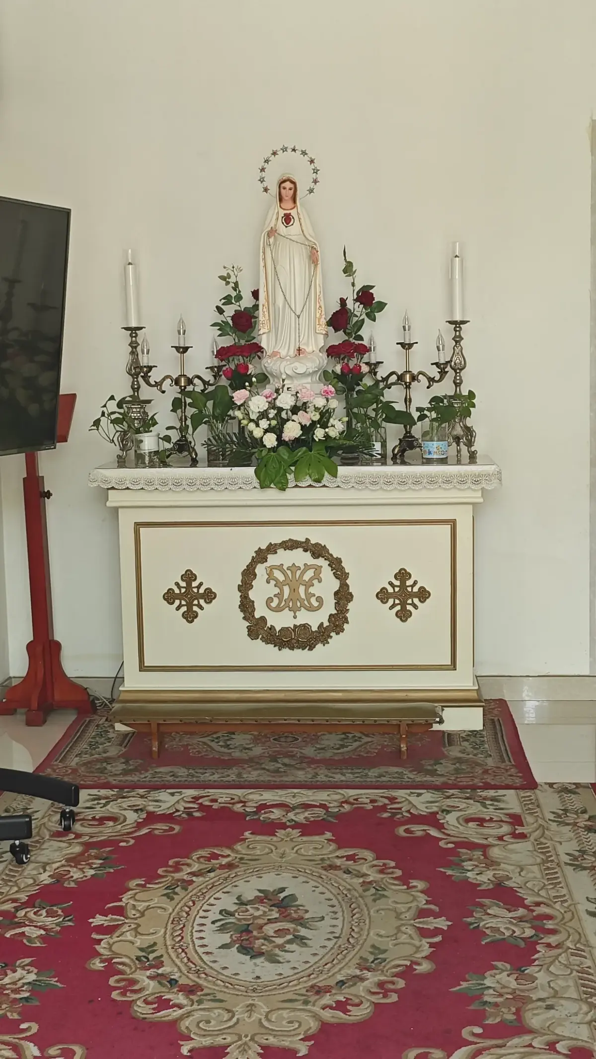 A white altar with candles, roses and a statue of Mary.
