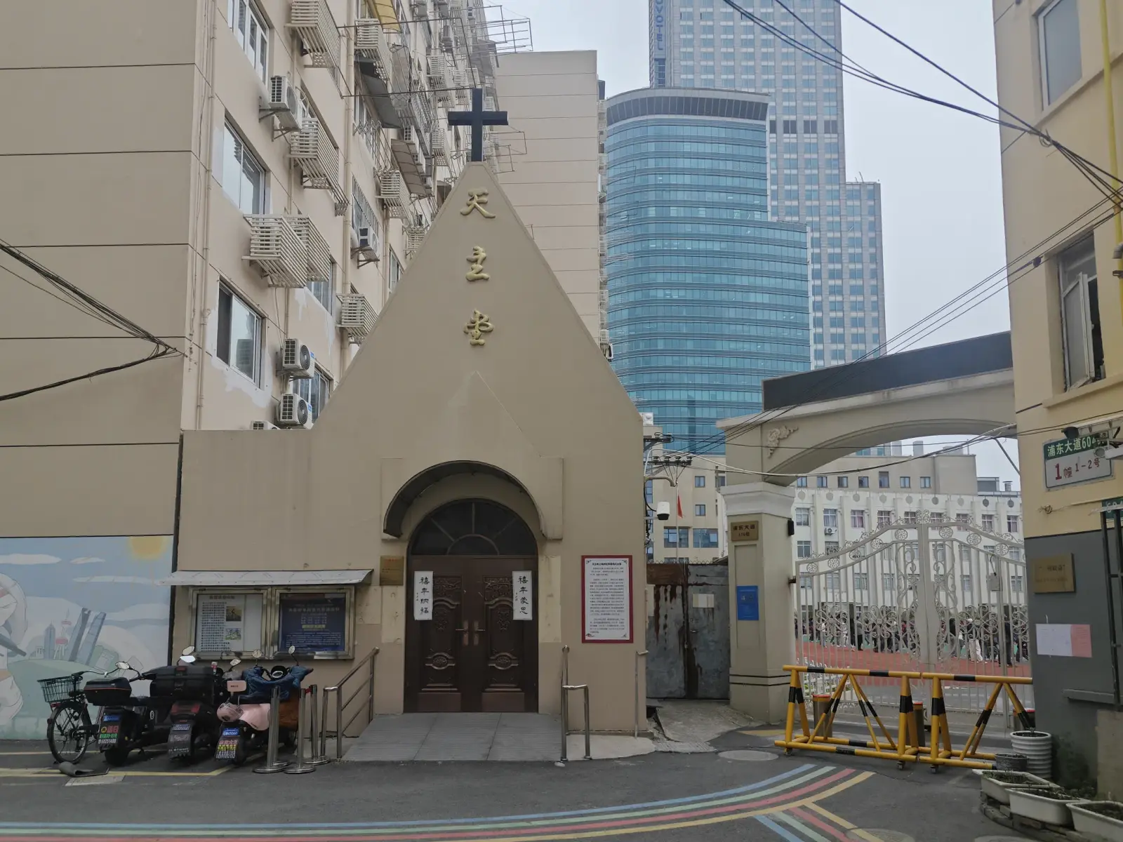 A small beige church front with a cross and gold Chinese characters between tall apartment buildings, with a glass tower behind.