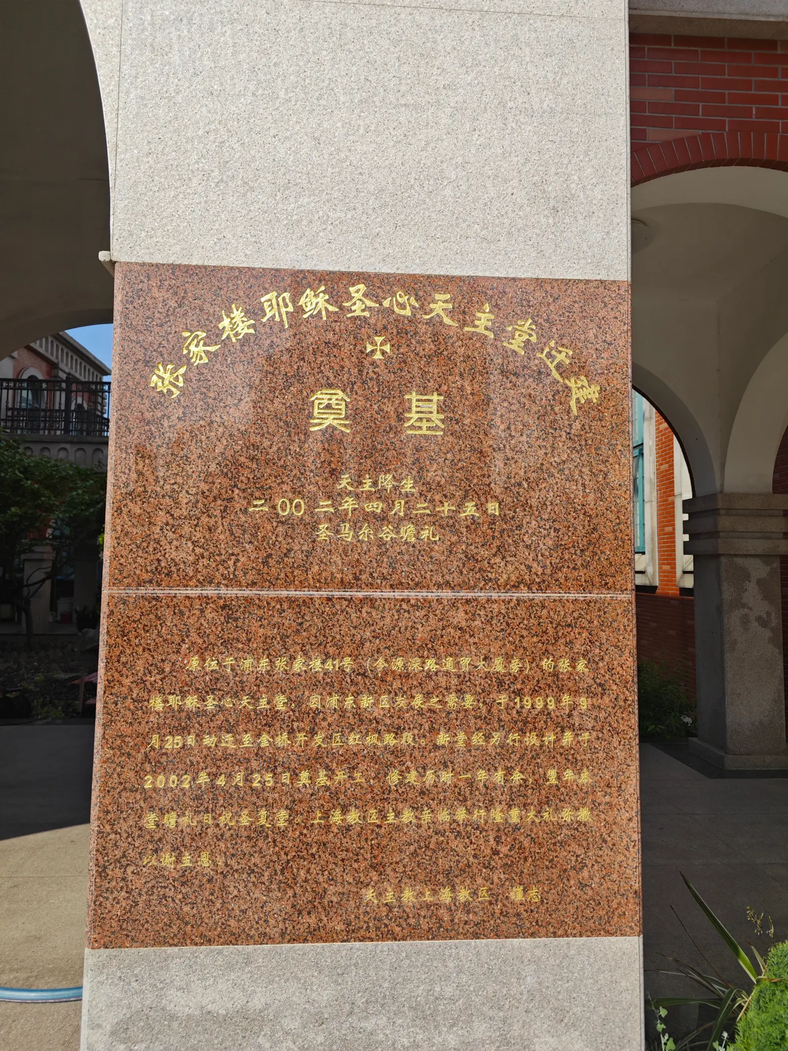 A polished red-brown granite tablet with gold Chinese characters, mounted on a pale stone pillar.