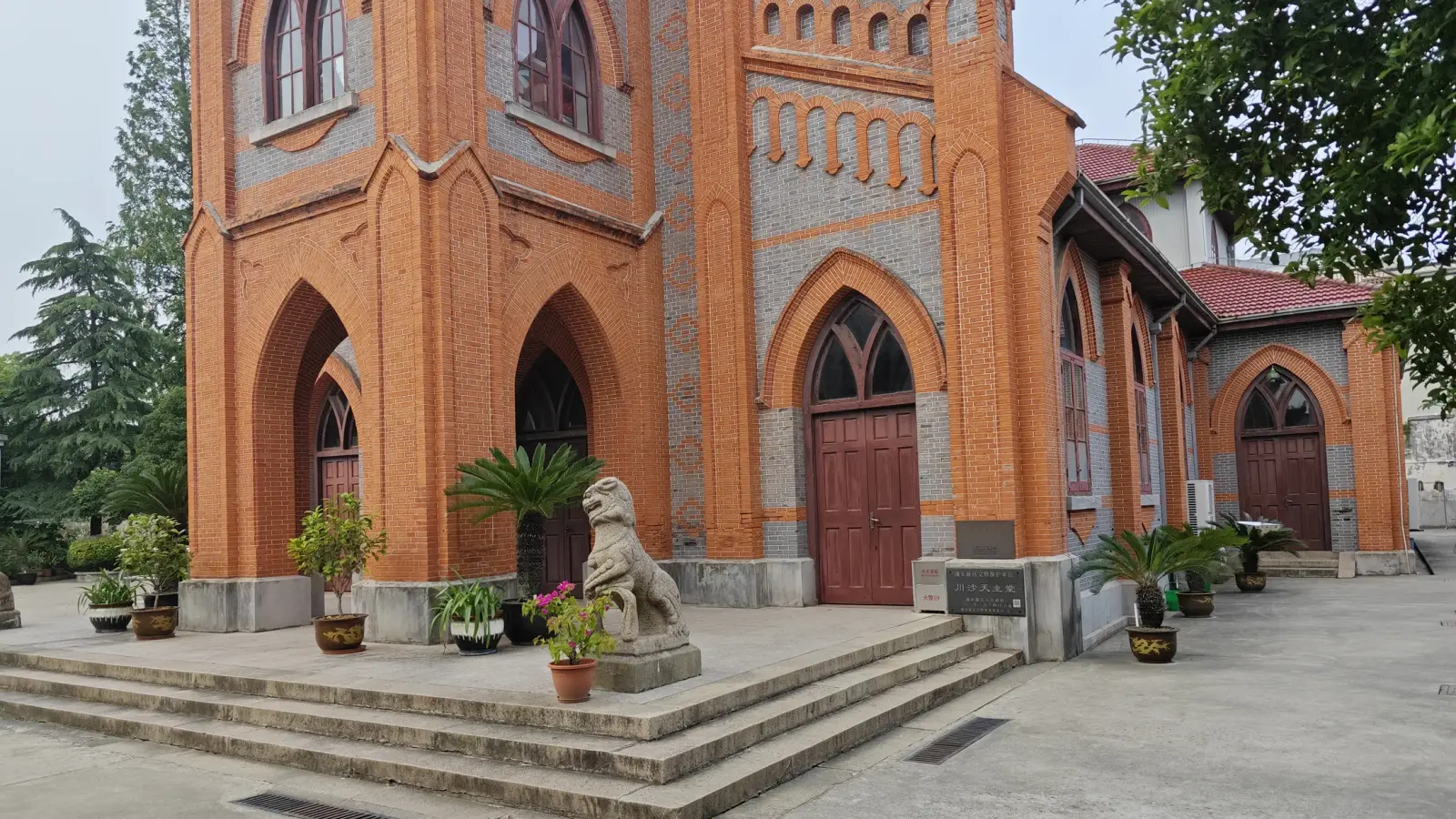 Orange brick tower base with pointed doorways, a stone lion statue and potted palms at the top of broad stone steps.