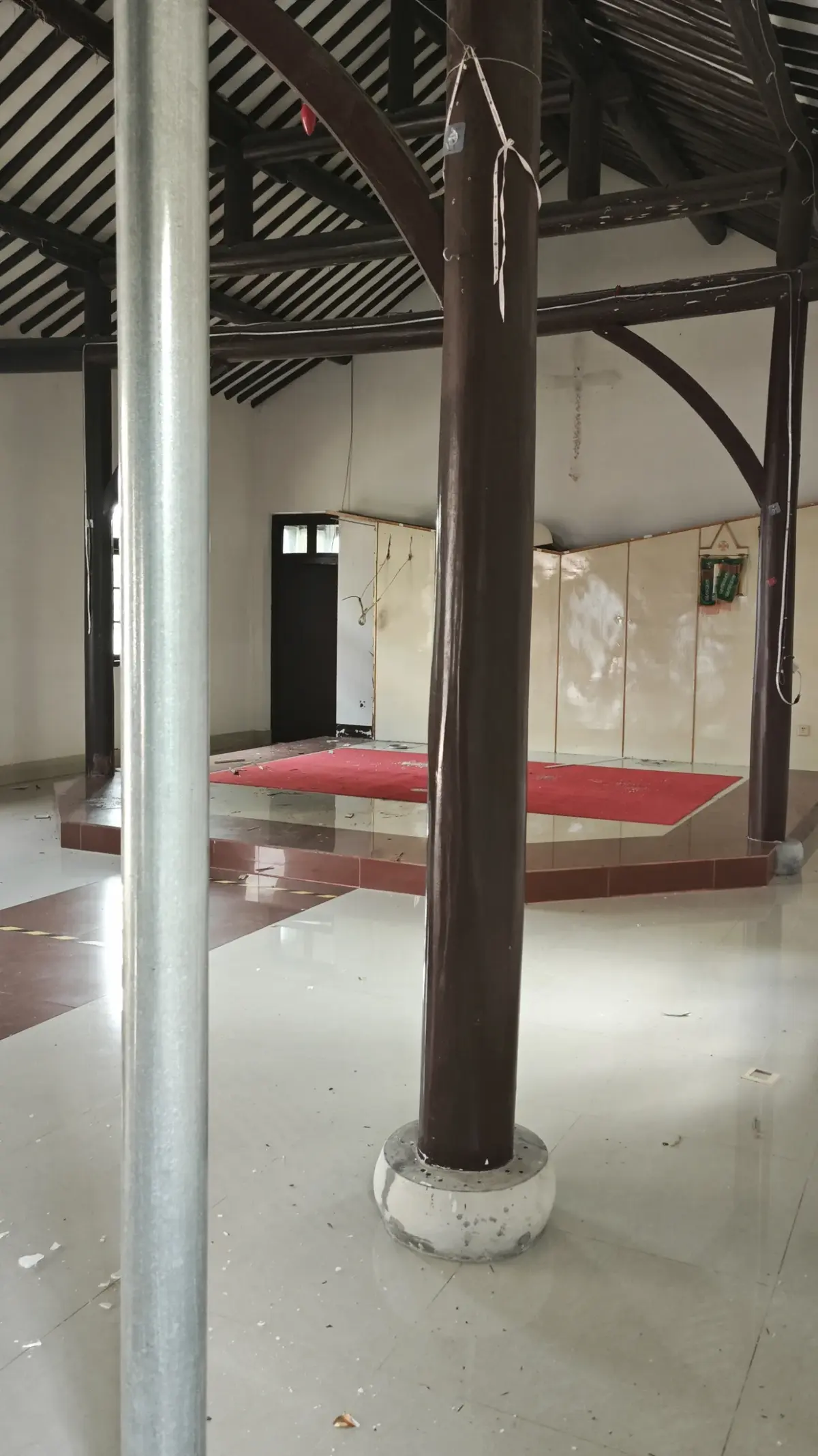 A large room with dark timber columns, exposed roof rafters and a red-carpeted platform at the far end.