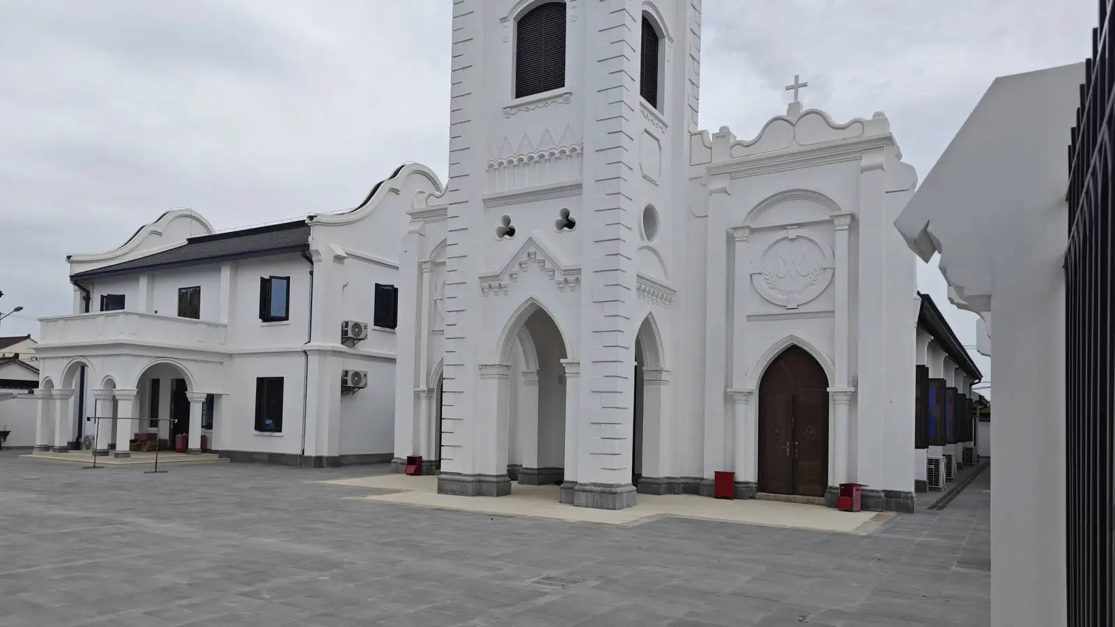 A white church front with a tower and pointed arched doorways next to a white two-storey building with a round-arched porch.