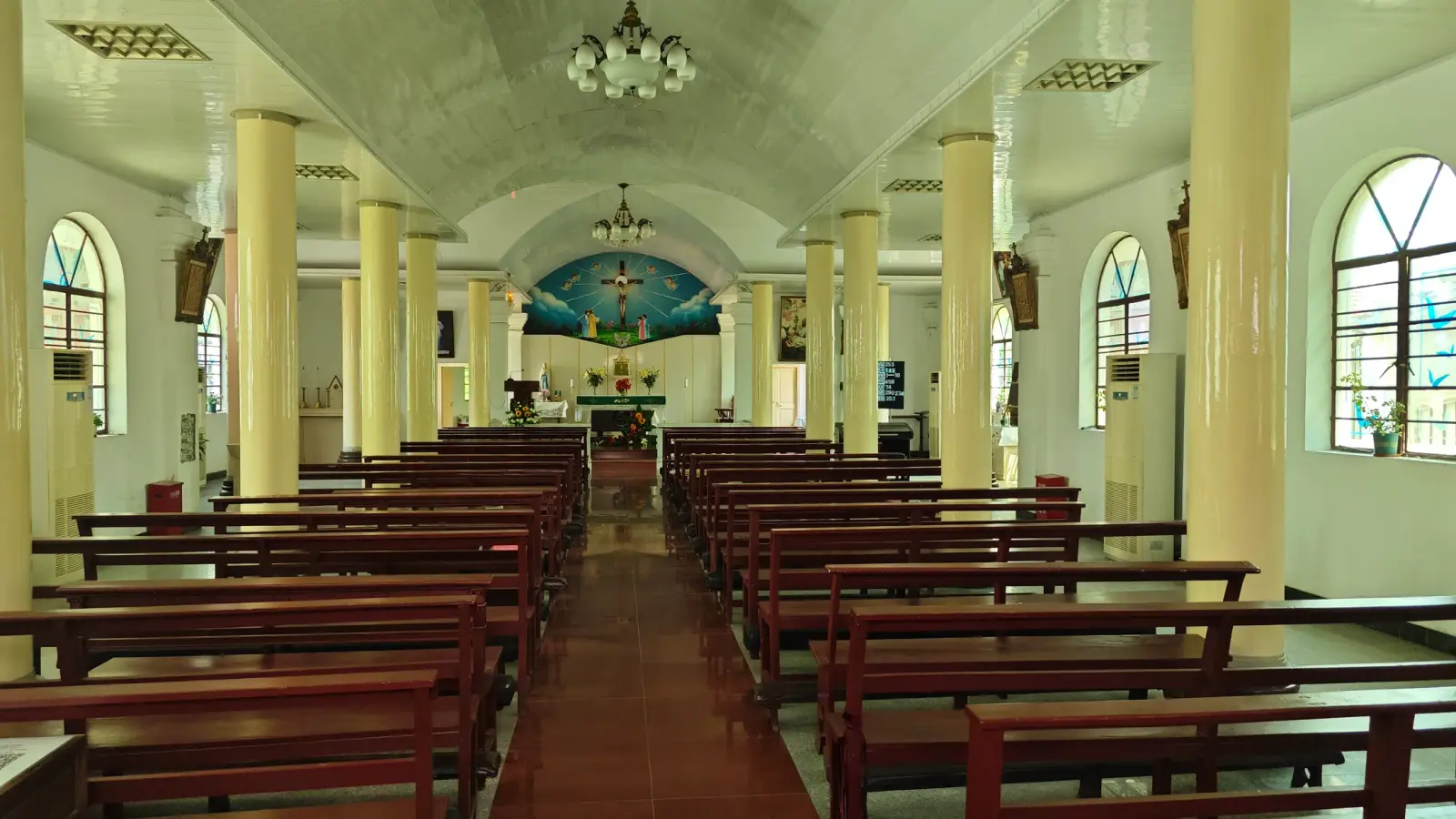 A church nave with tall cream columns, arched windows, red-brown pews and a blue painted apse at the far end.
