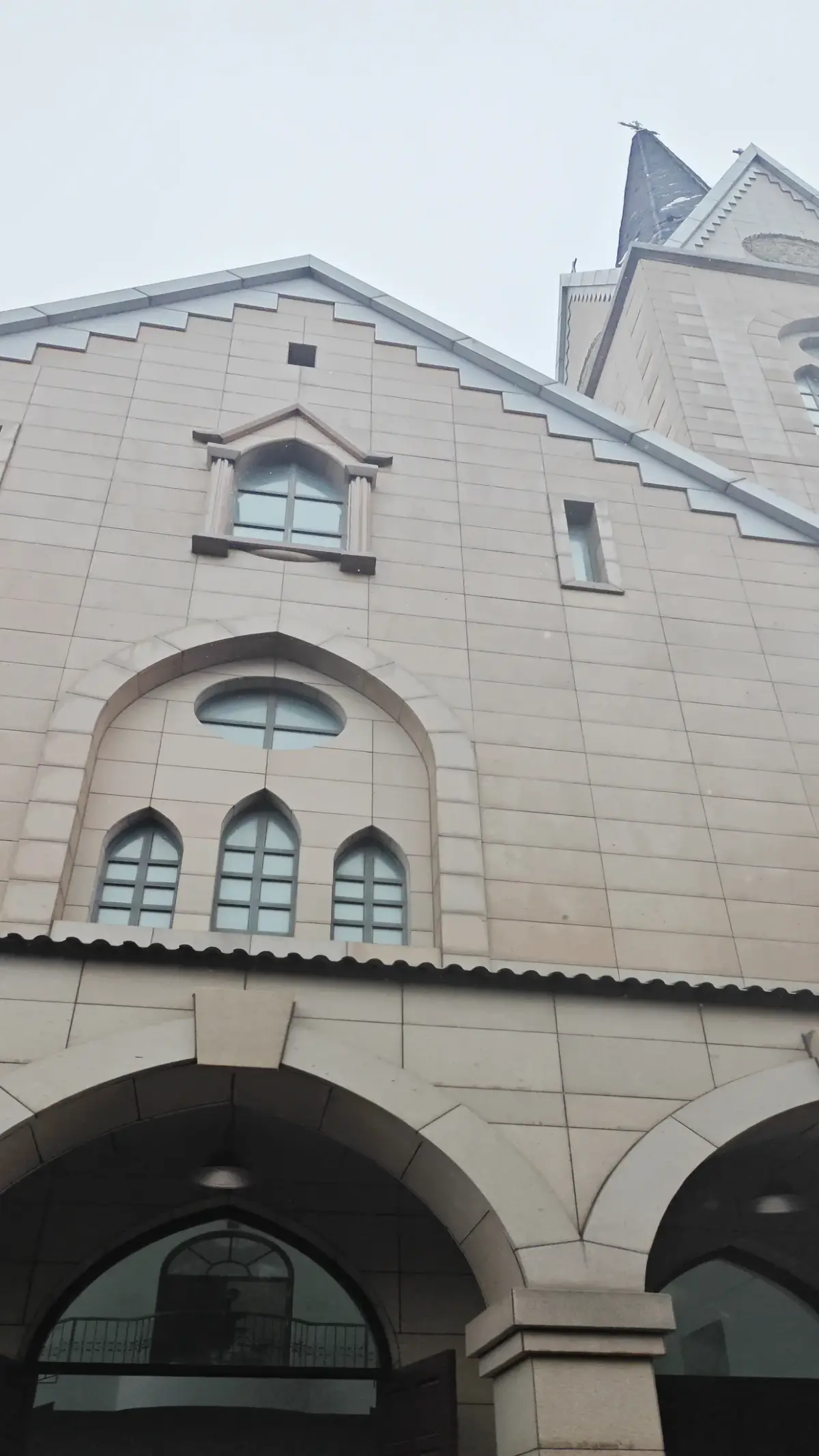 Looking up at a stone church front with a stepped gable, three small pointed windows, and large arches at the entrance.