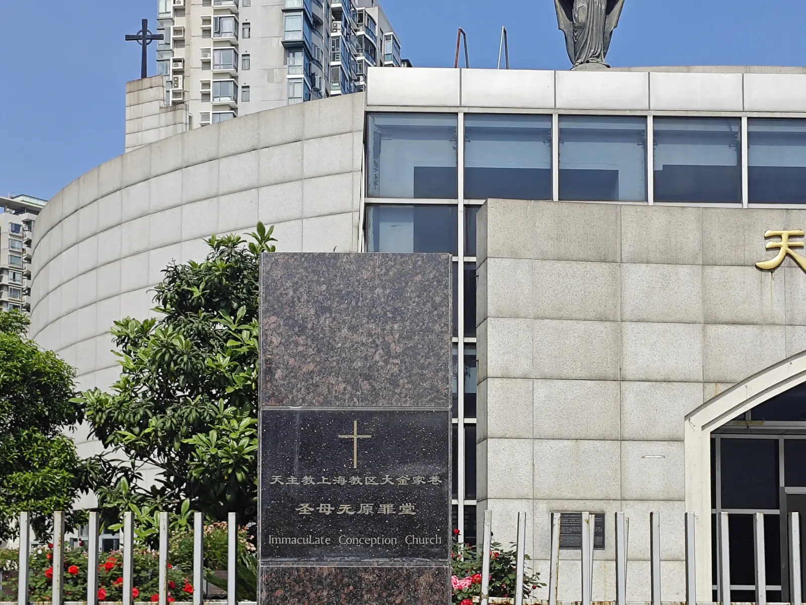 A dark granite post with a cross and the words Immaculate Conception Church in front of a curved stone church wall.