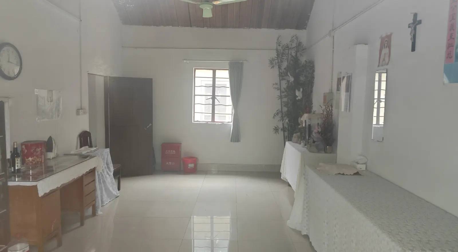 A bright, plain room with white walls, a timber ceiling, a crucifix on one wall and tables at the sides.