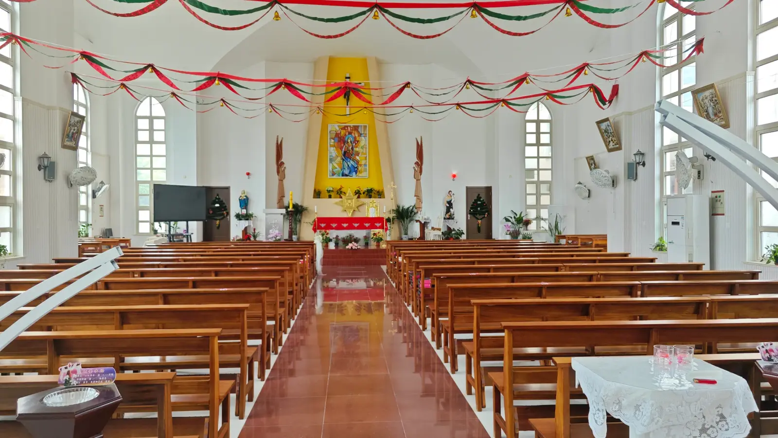 A bright church interior with wooden benches, a polished red aisle and red and green streamers hung from the ceiling.