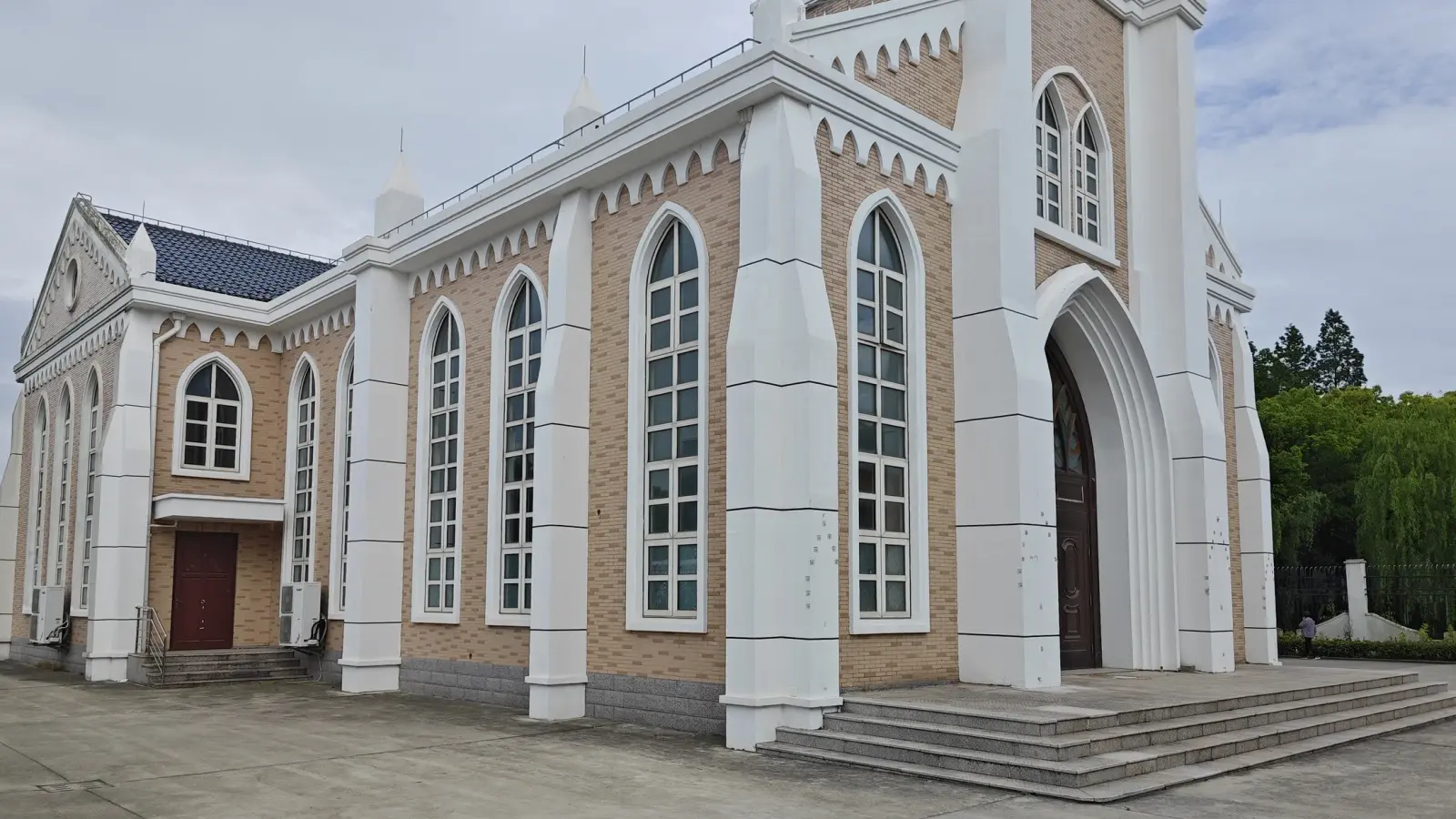 A brick church seen at an angle with white buttresses, tall pointed windows and wide entrance steps.