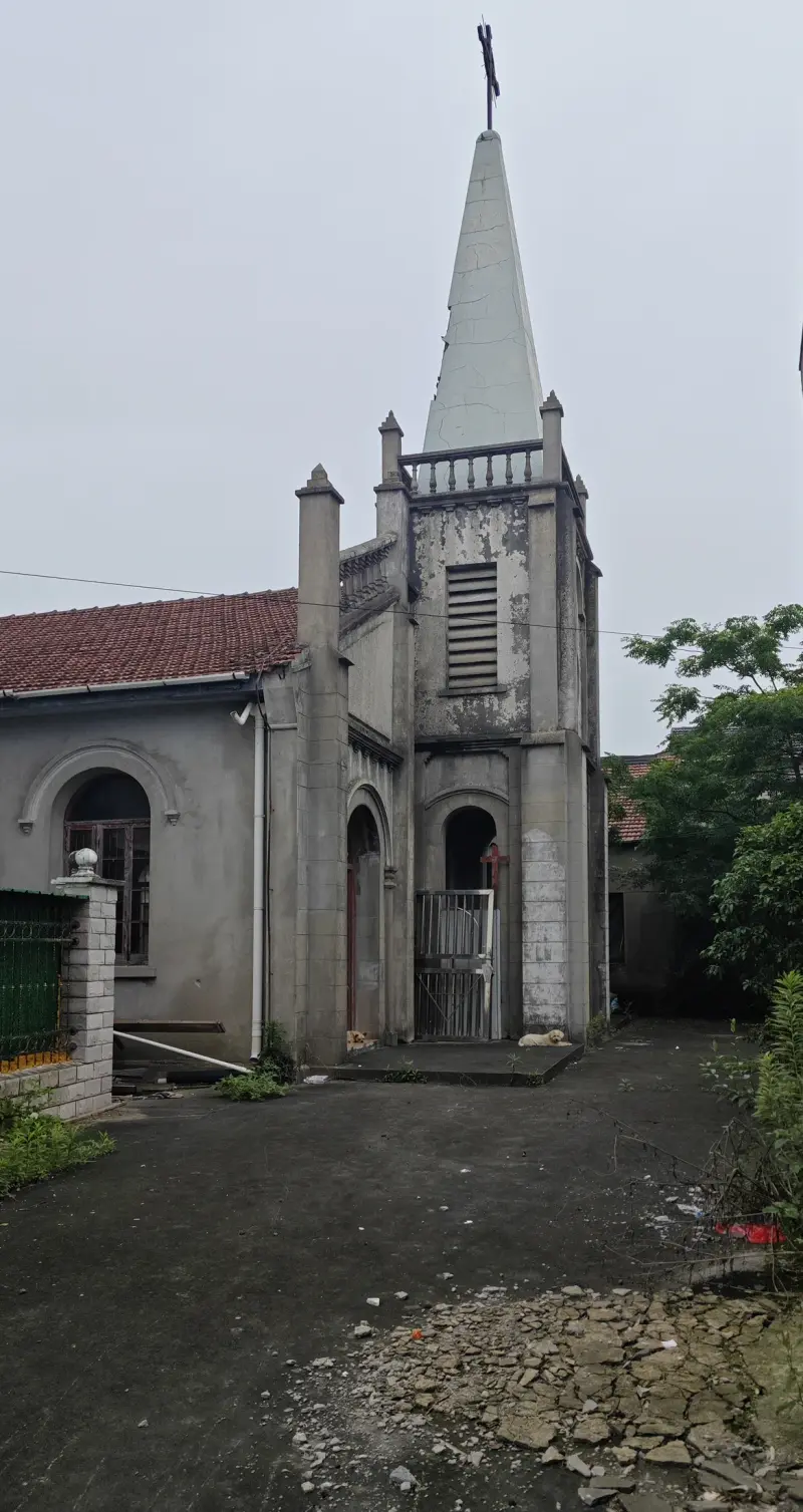 A pointed tower rises behind a passage between walls, with arched windows on the church beside it.