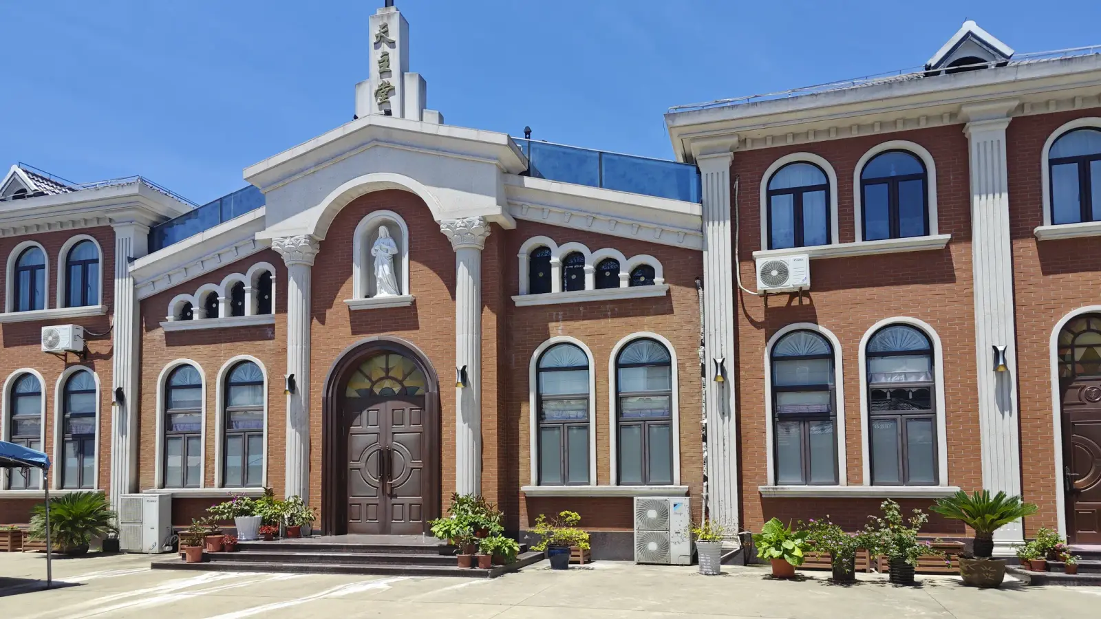A two-storey red brick church front with white pilasters, arched windows, a central pediment with a statue niche and Chinese characters, and a carved wooden door.