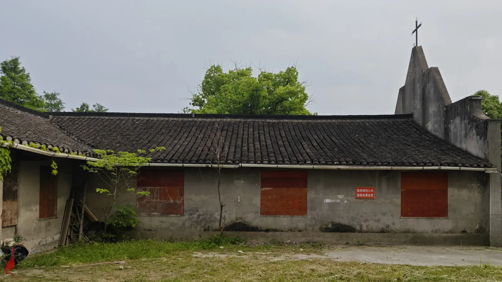 A long grey building with a dark tile roof, red boarded windows and a stepped gable topped with a cross.