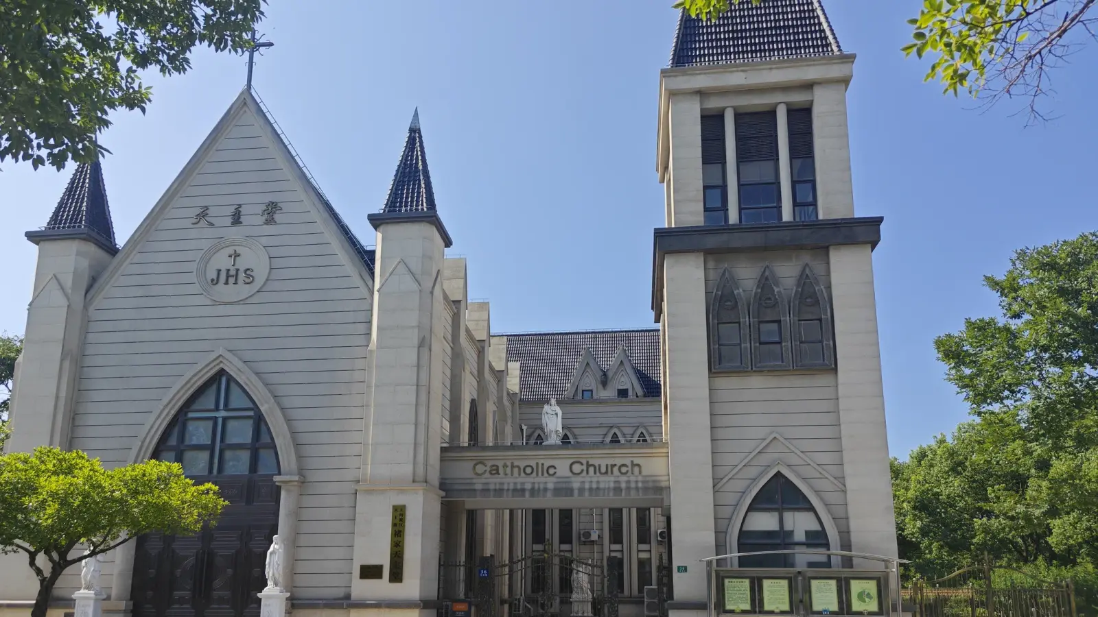 A grey neo-Gothic church with a pointed gable, a square tower and a sign reading Catholic Church above the porch.
