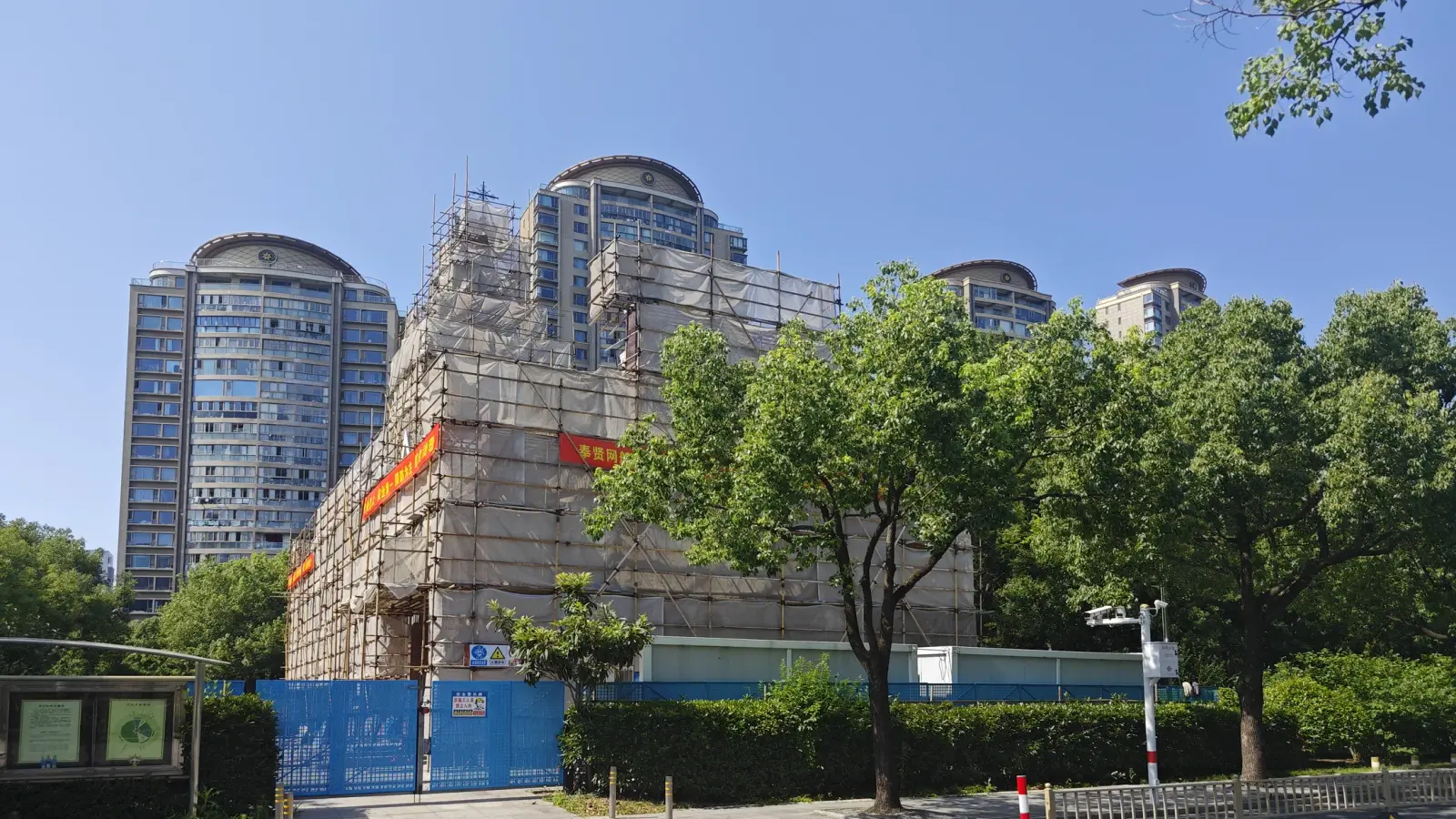 A church building fully covered in scaffolding with red banners, with apartment towers behind.