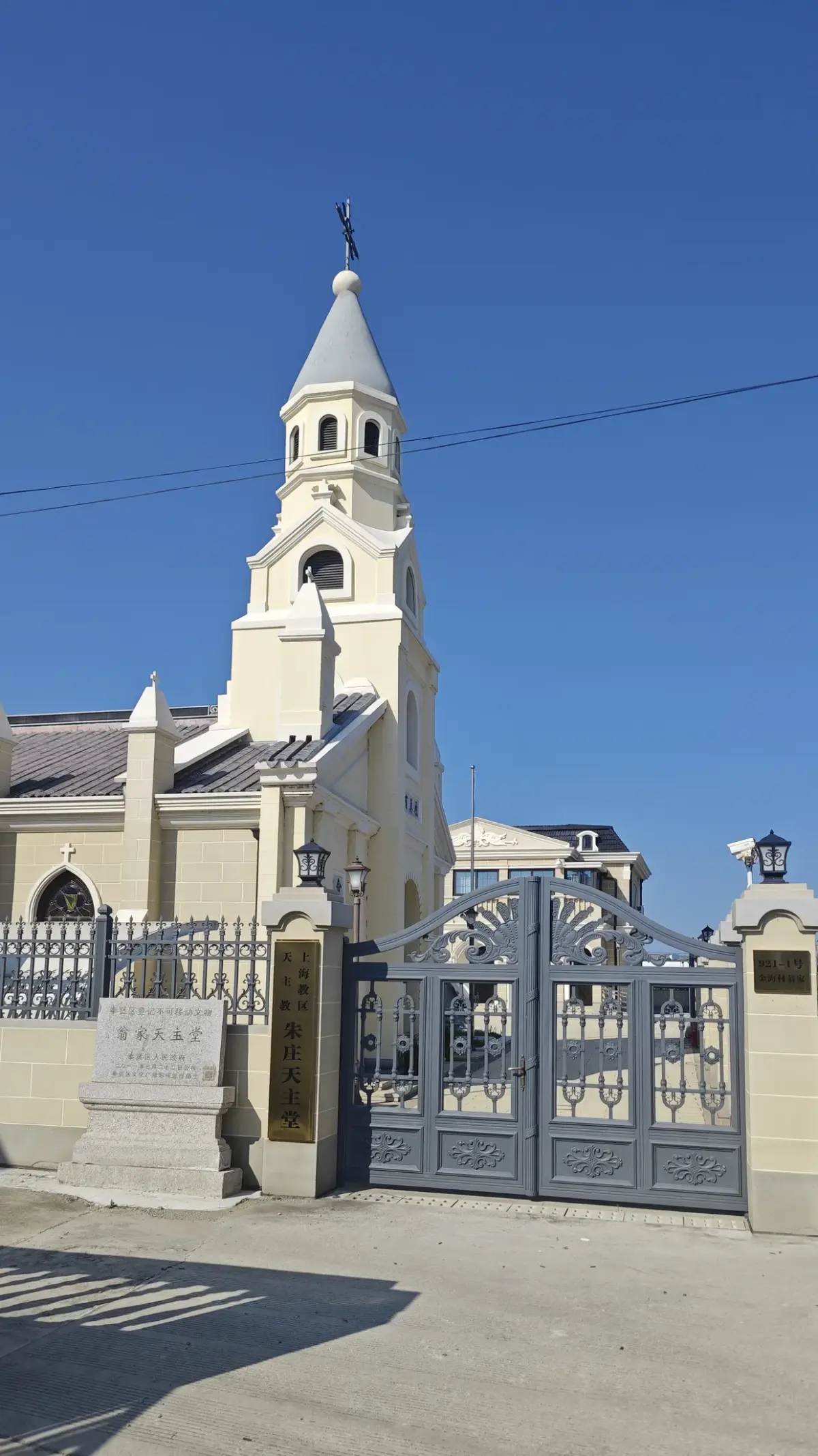 Cream church steeple behind a grey iron gate, with a stone plaque beside the gatepost.