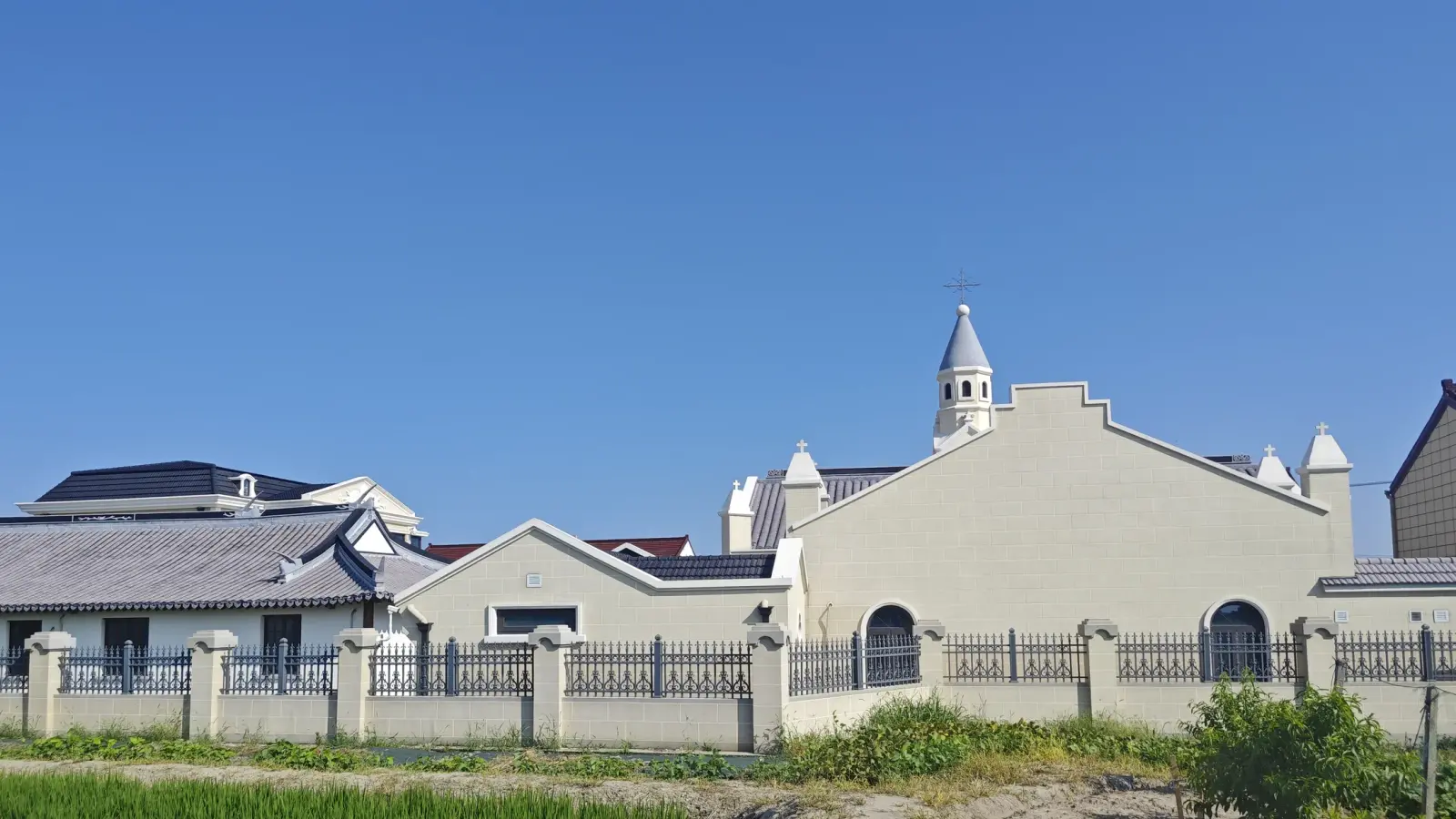 Cream church with stepped gable and small spire above a fence and green field.