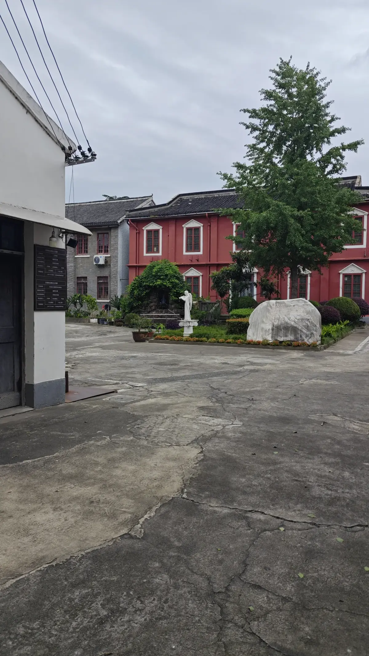 Courtyard with a large tree and statue in front of a red-walled church.