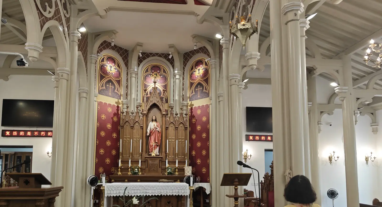 A carved wooden altar with a statue and red patterned panels between cream columns.
