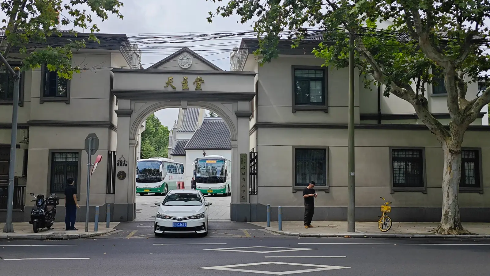 A grey archway between two buildings with Chinese characters above it, with buses and a car beyond on the street.