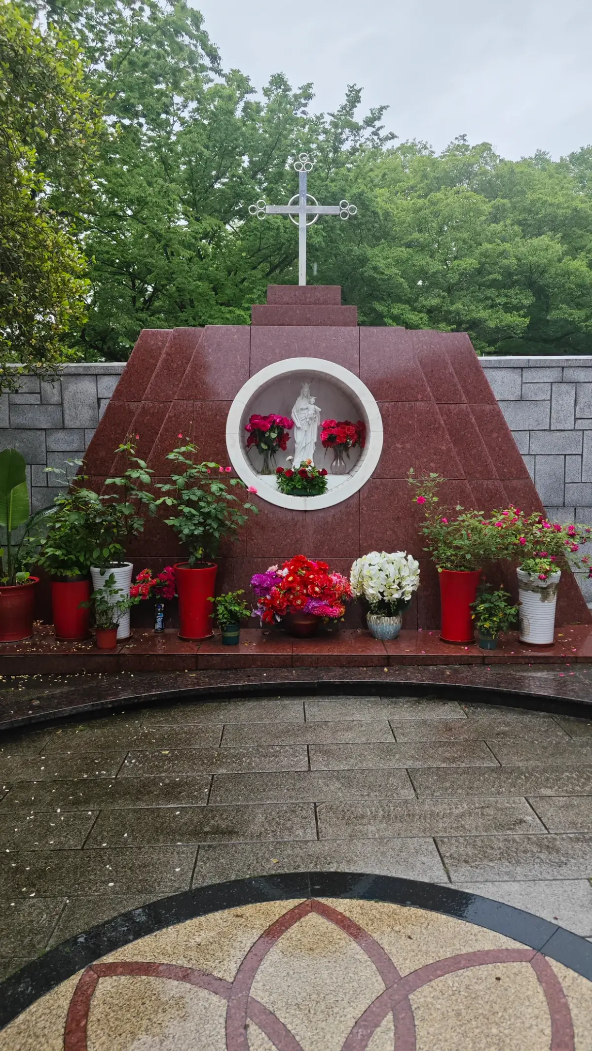 A red-toned wall with a round niche holding a white statue, and potted red flowers.