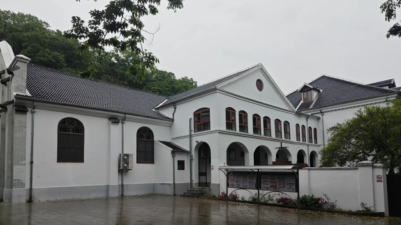 White buildings with arched windows and a grey tiled roof beside a wet courtyard.