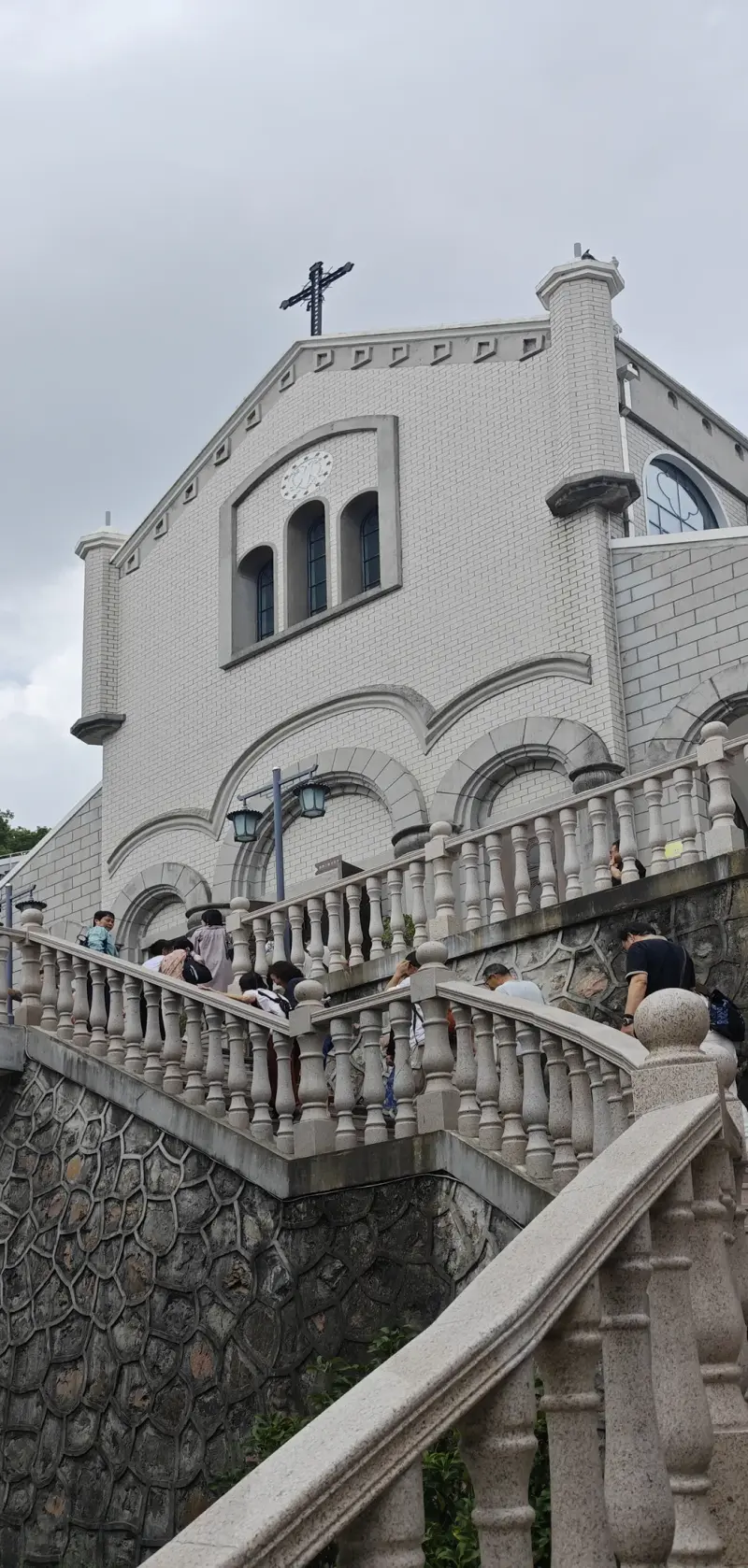 A white chapel at the top of a stone staircase with balustrades, with visitors on the steps.
